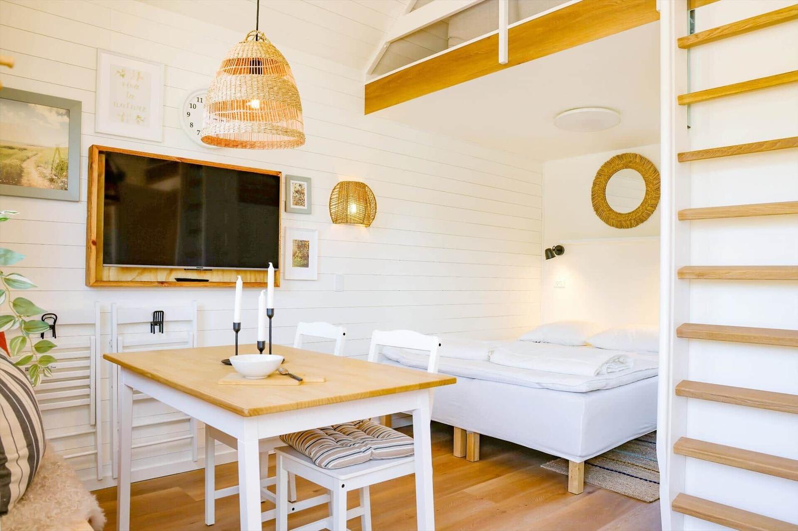 A room with a sleeping area, dining table, and TV mounted on the wall.