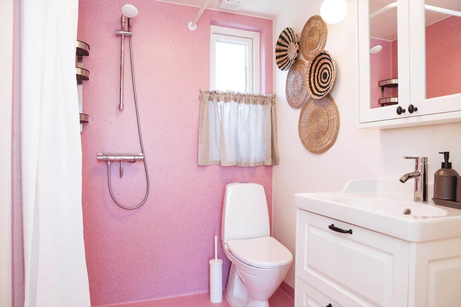 Bathroom with pink walls, toilet, shower, and sink with mirror cabinet.