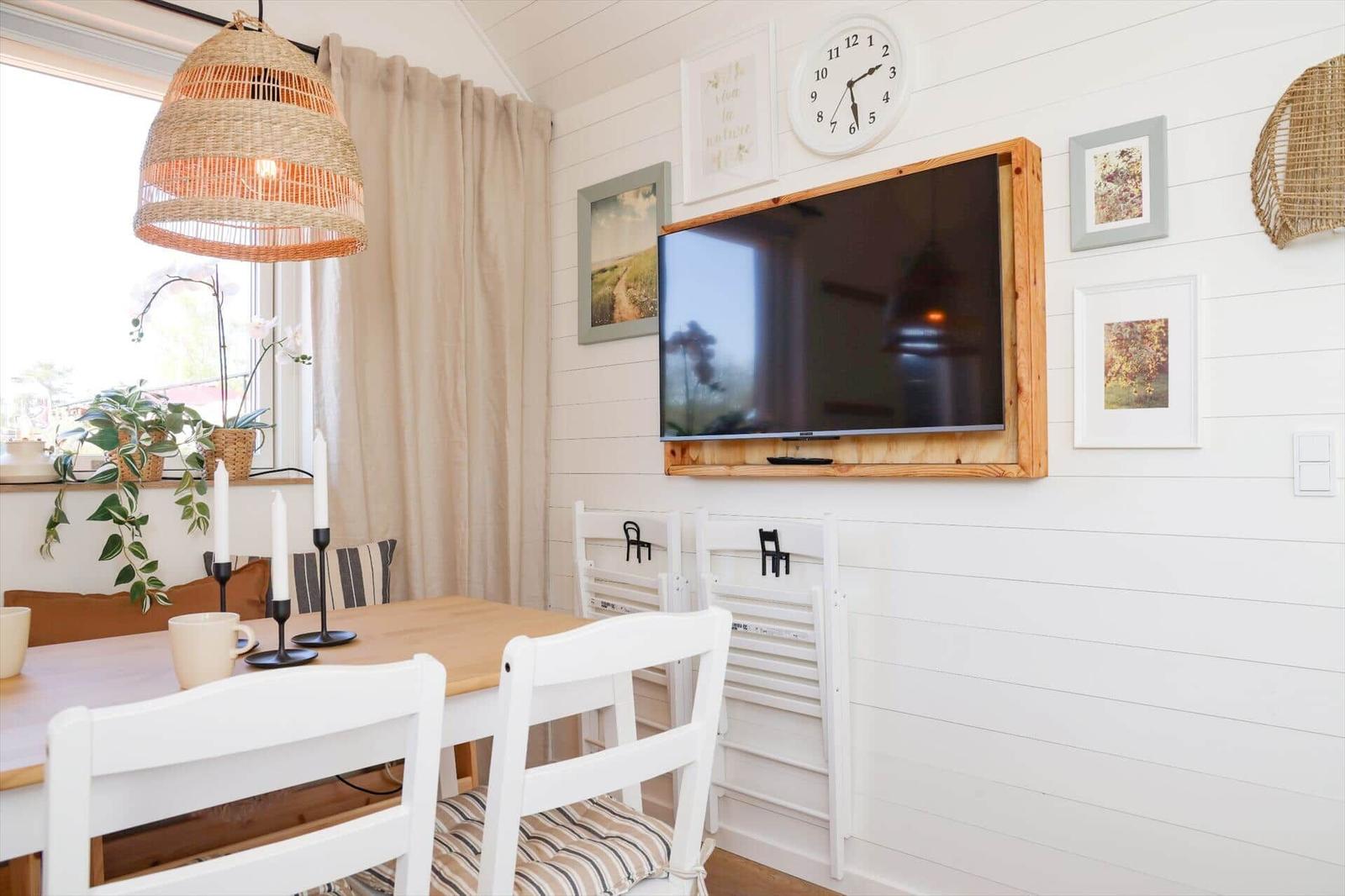 Dining room with table, chairs, wall clock, and TV in wooden frame.