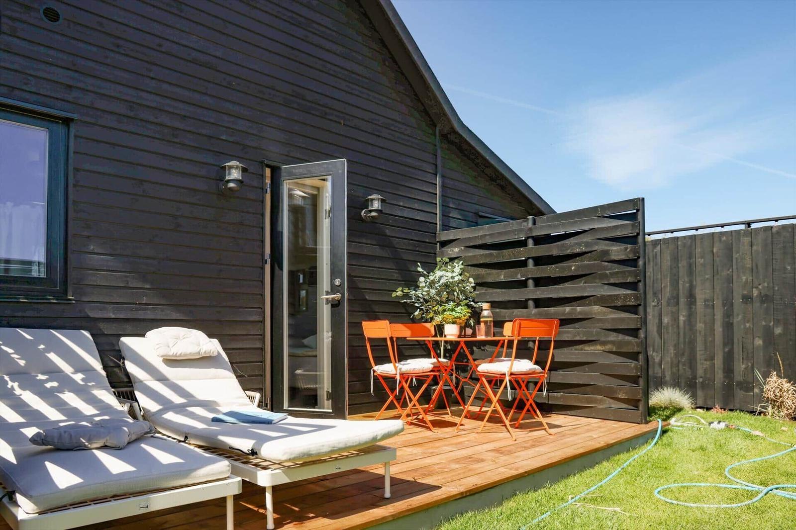 Deck with loungers and orange table set in front of a dark wood house.