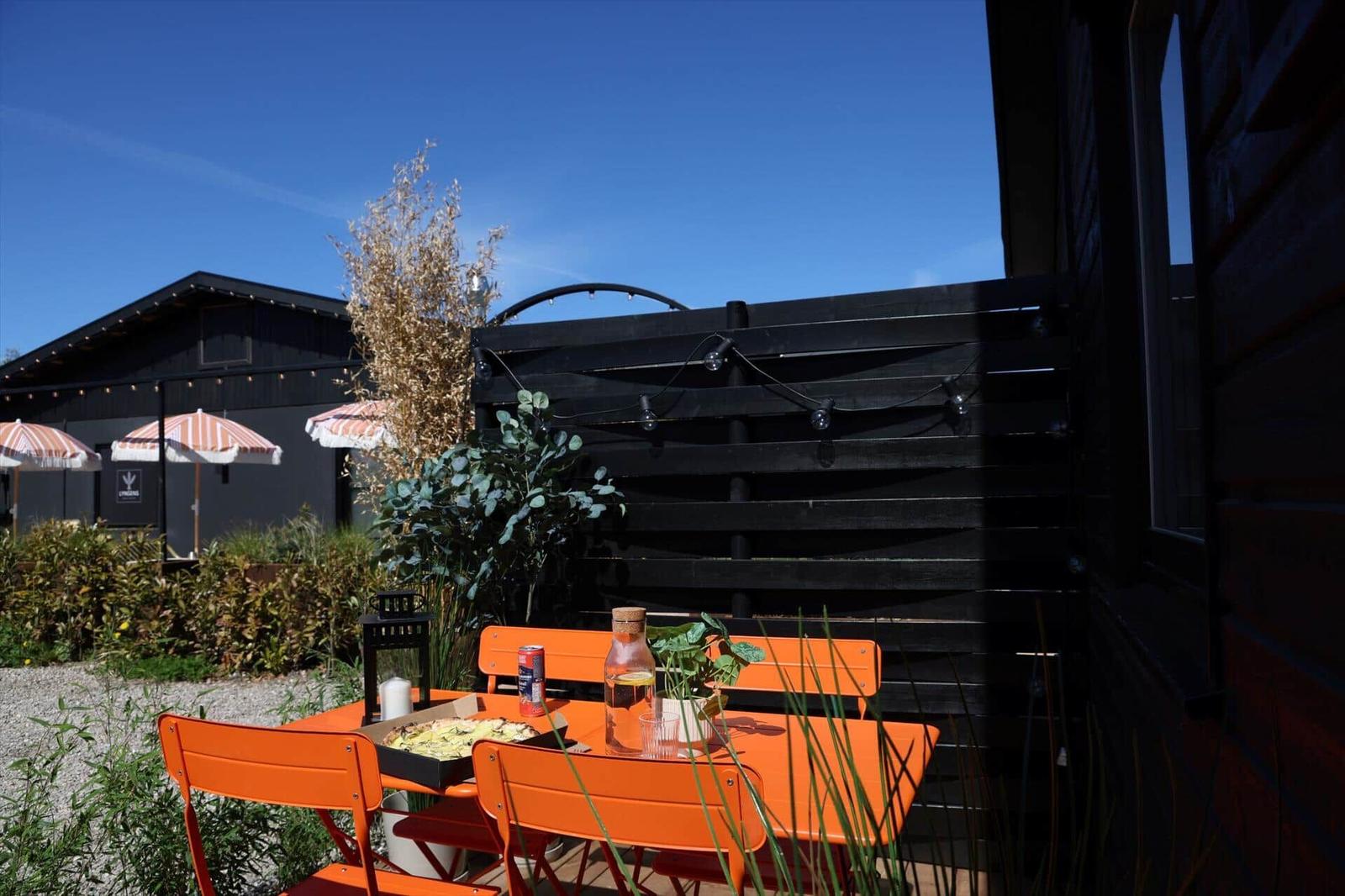 Orange table and chairs on terrace with plants and background house.