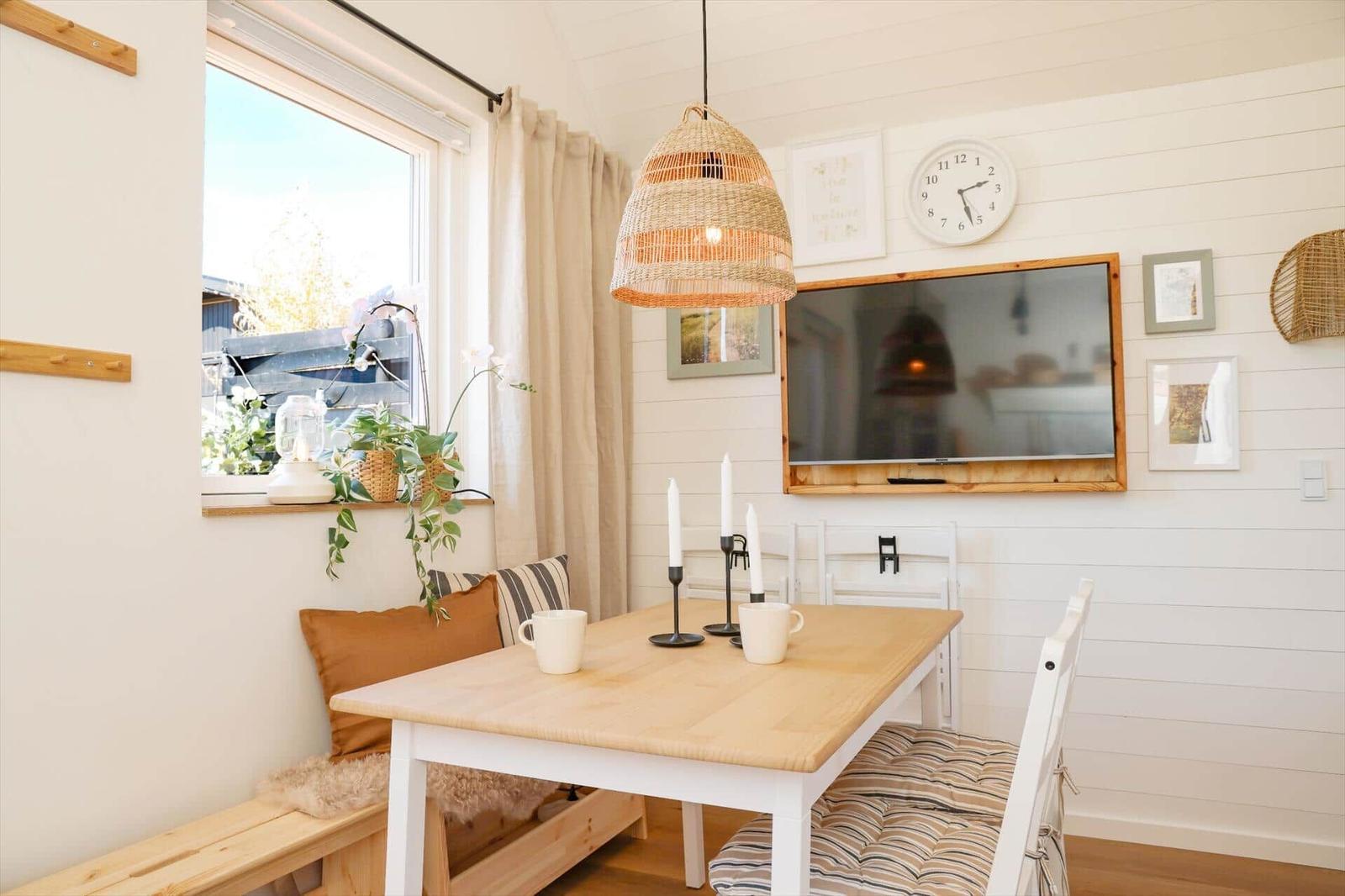 Dining table with chairs, wall clock, and TV on white wall.