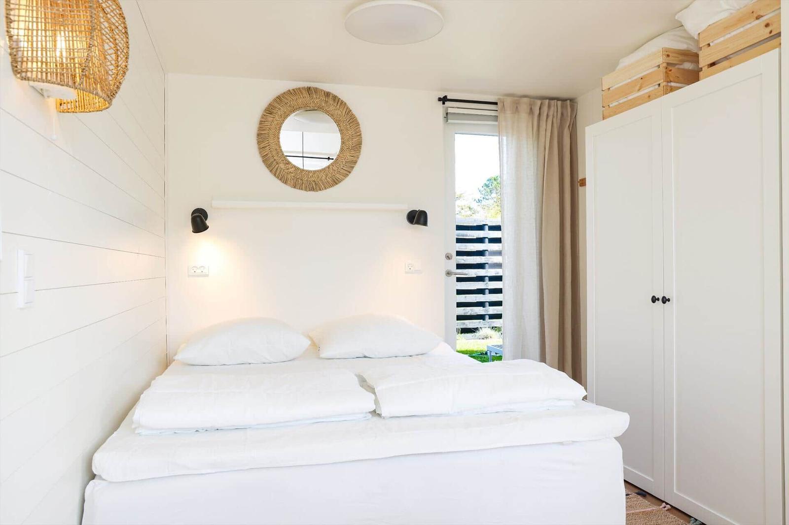 Bedroom with white bed, wall mirror, and wardrobe. Door leads outside.