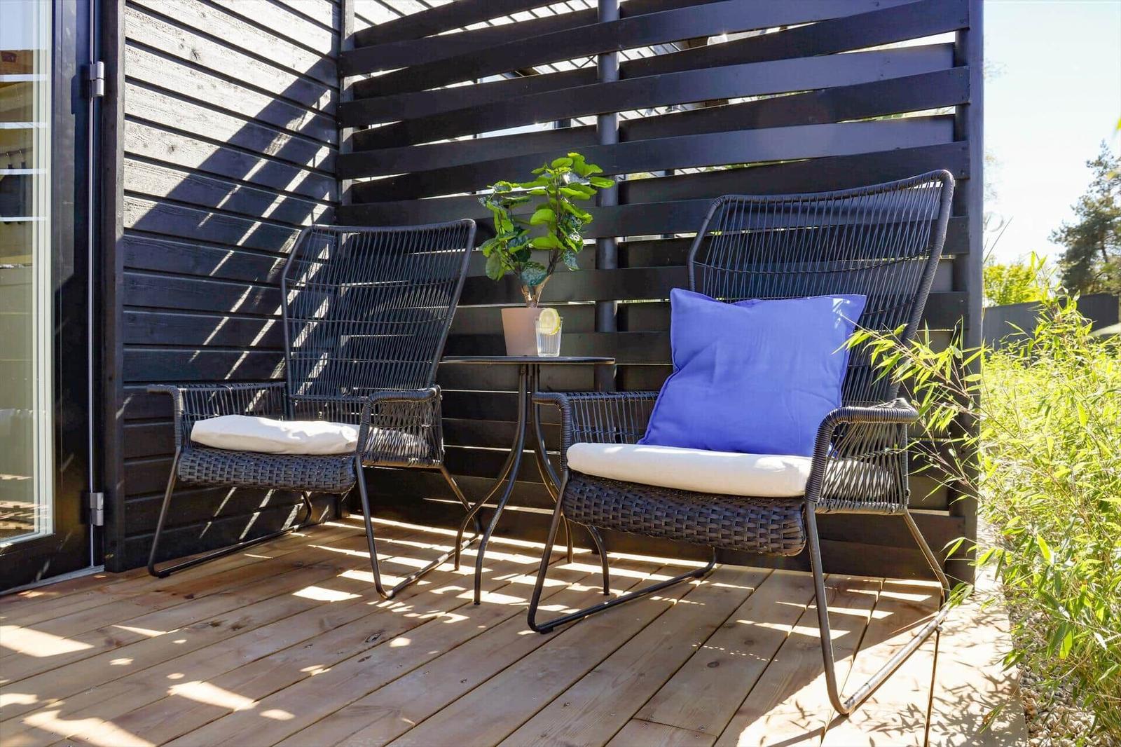 Deck with two chairs, table, and plant against dark wooden wall.