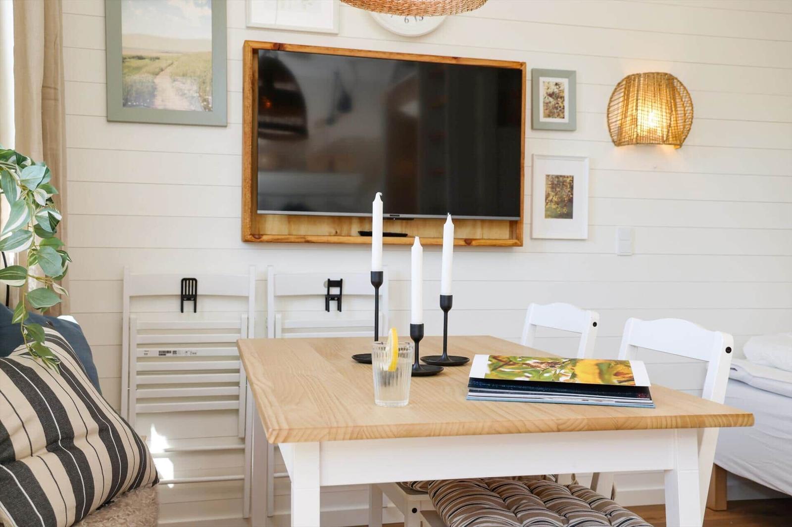 Dining room with wooden table, white chairs, and TV mounted on the wall.