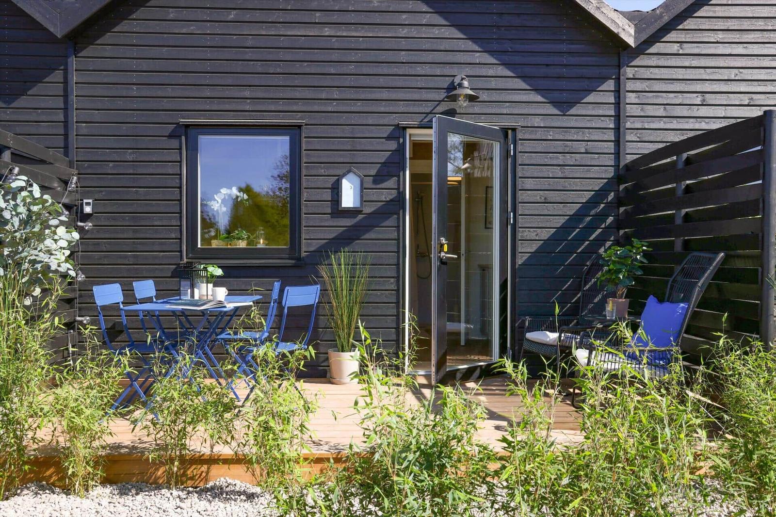 Terrace with table, chairs, and seating area in front of a house with dark wooden facade.