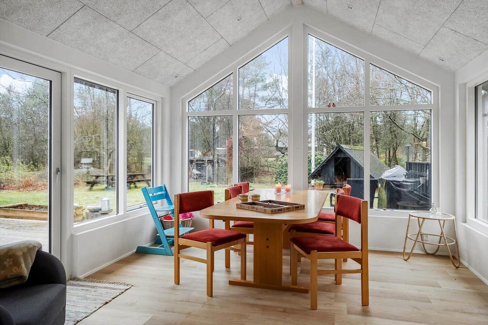 Dining room with wooden table, red chairs, and large windows overlooking the garden.