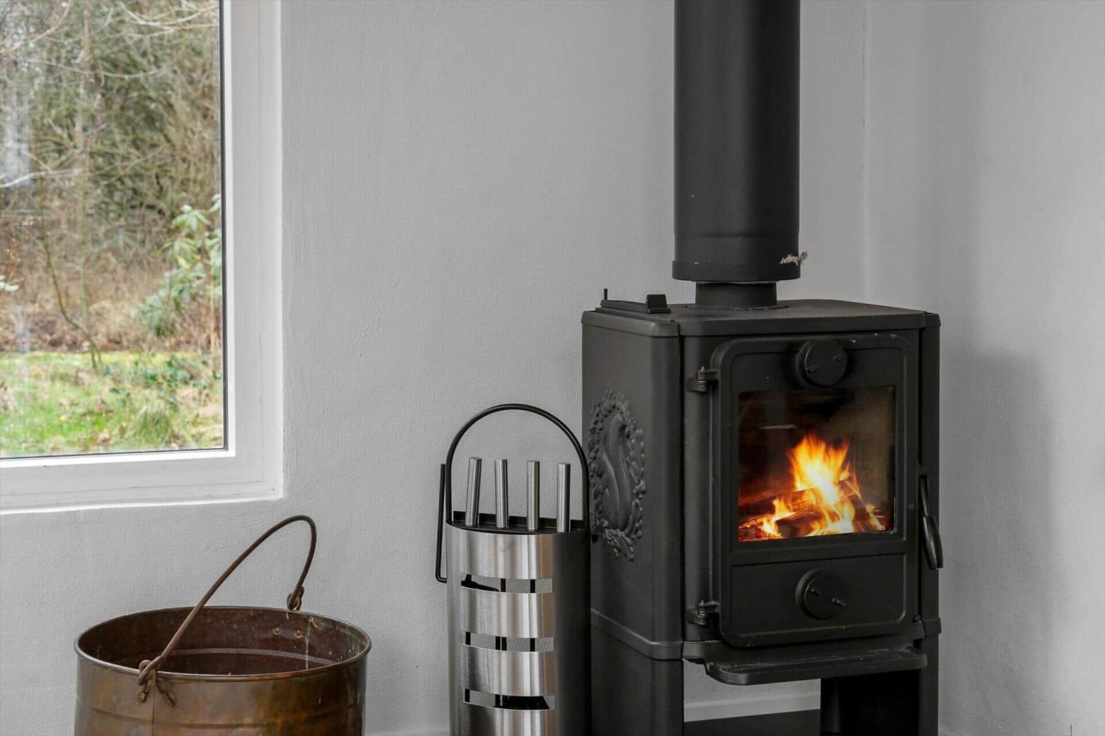 Wood stove with burning fire next to window and tool holder