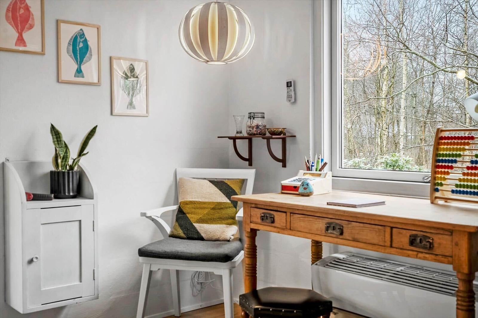 A workspace with wooden desk, chair, and window view of forest.