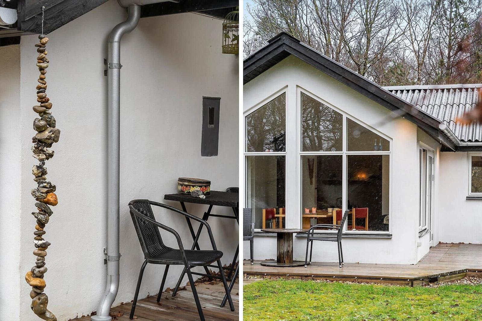 Outdoor area with stone column, table, and chair. Modern house with large window and terrace.