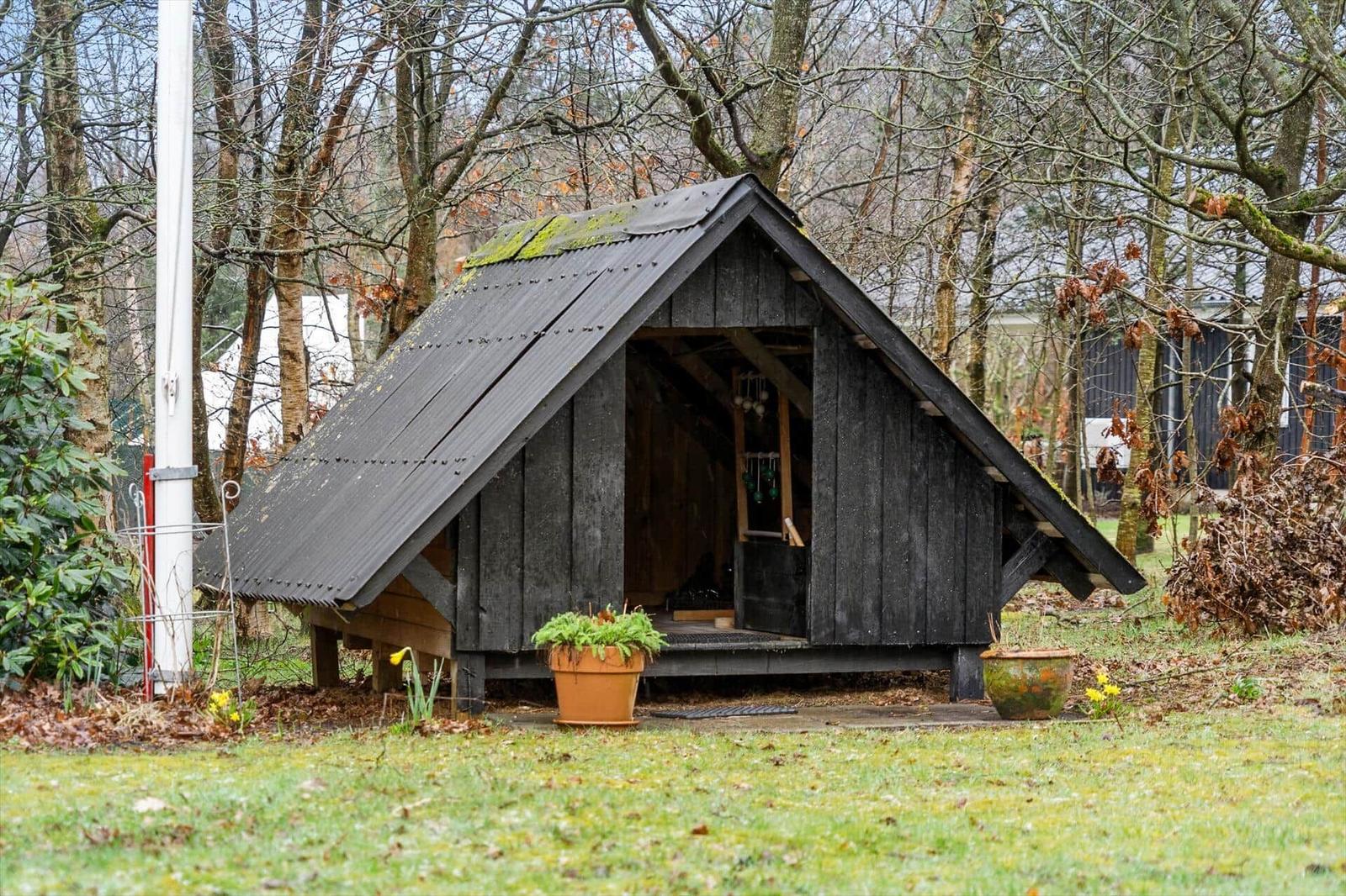 Wooden cabin with corrugated metal roof and potted plants in front yard.