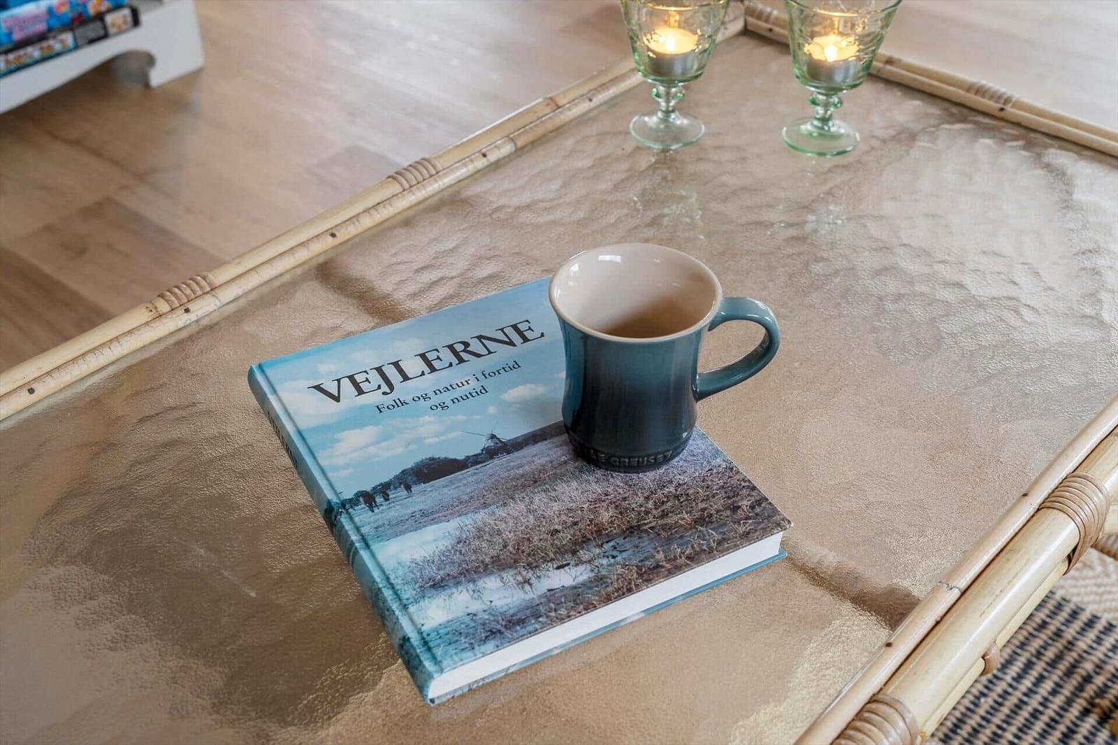 On a glass table, a book and a mug with tea are placed. Two candle holders are also on it.