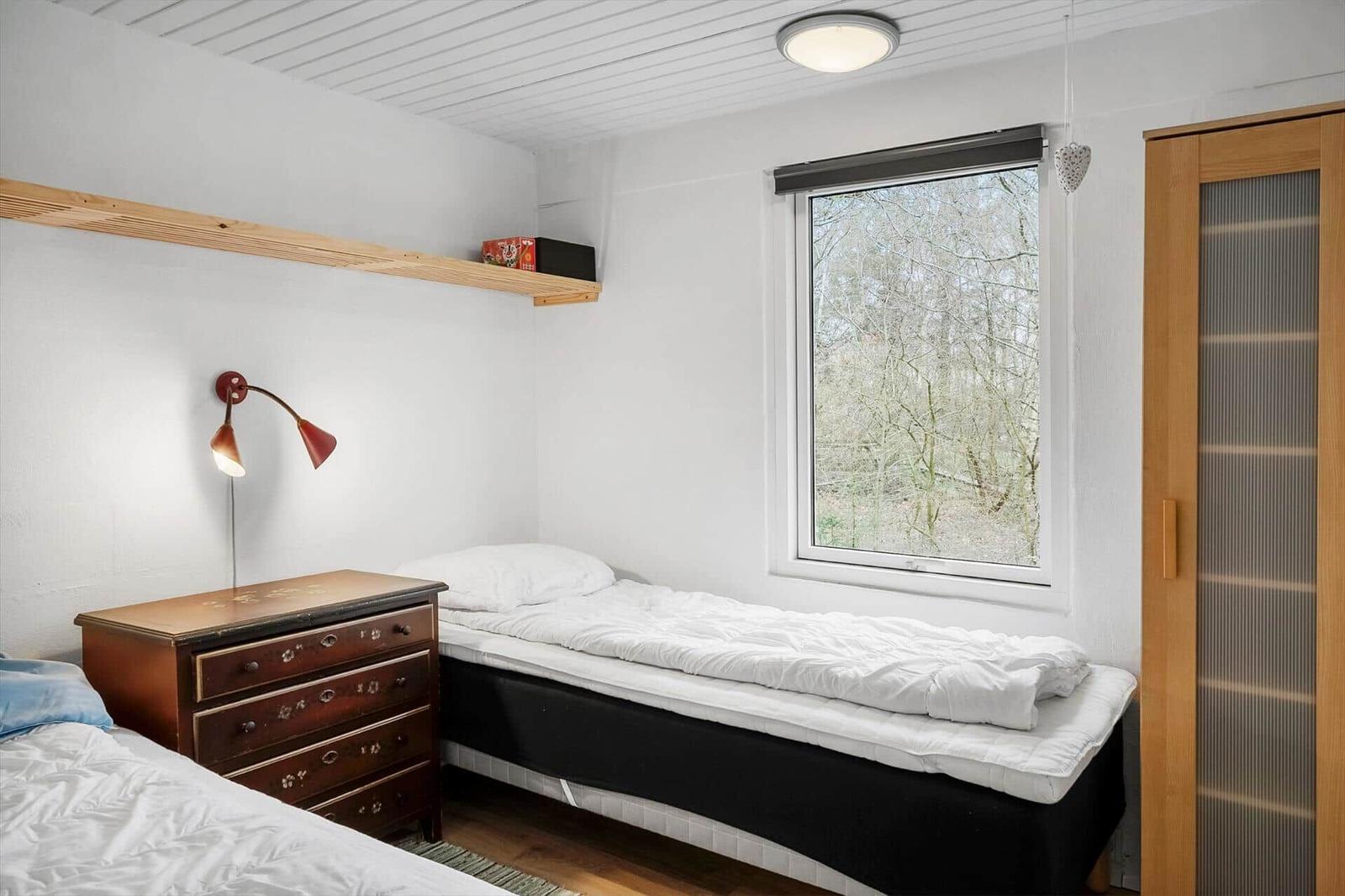 Bedroom with two beds, wardrobe, and window with view of trees.