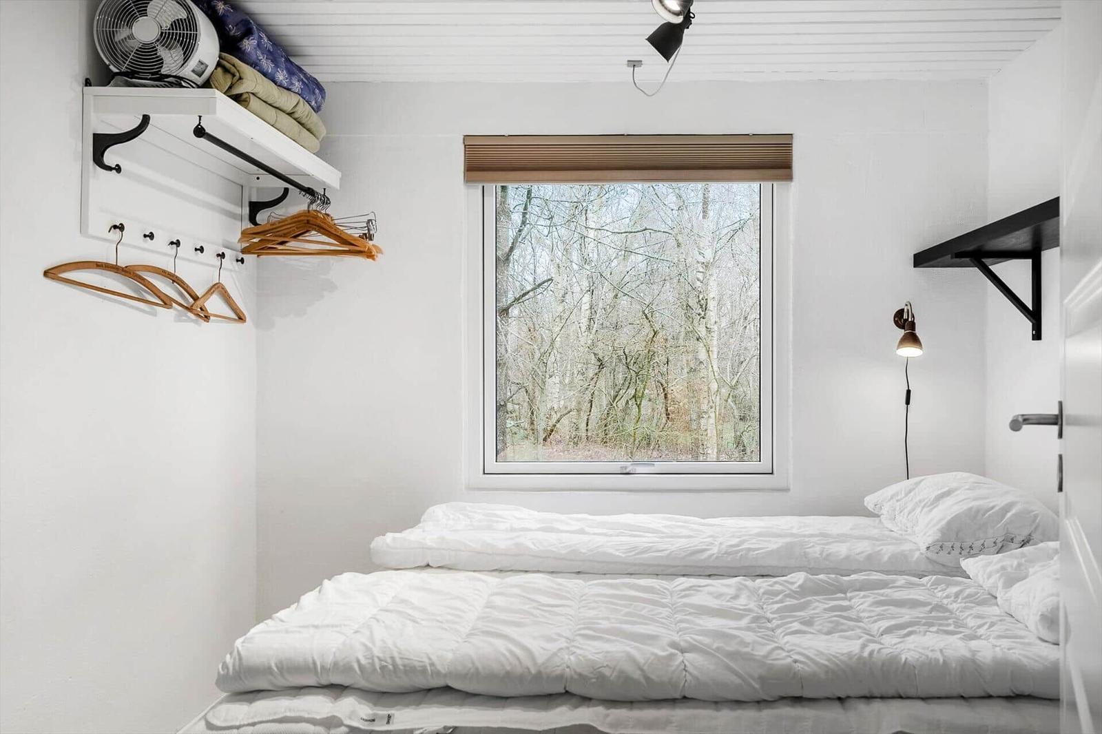 Bedroom with bed, window, and shelf. Trees outside. Ceiling fan and wall lamp.