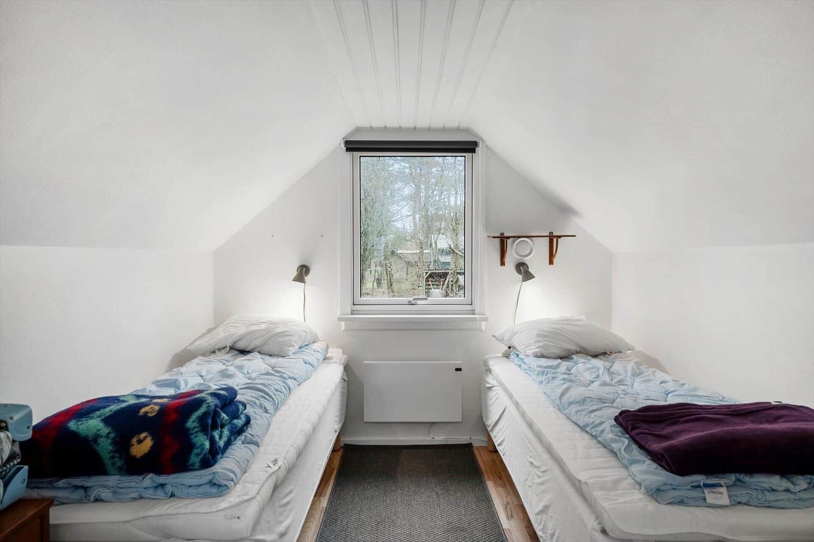 Two single beds under a dormer window with a view of trees.