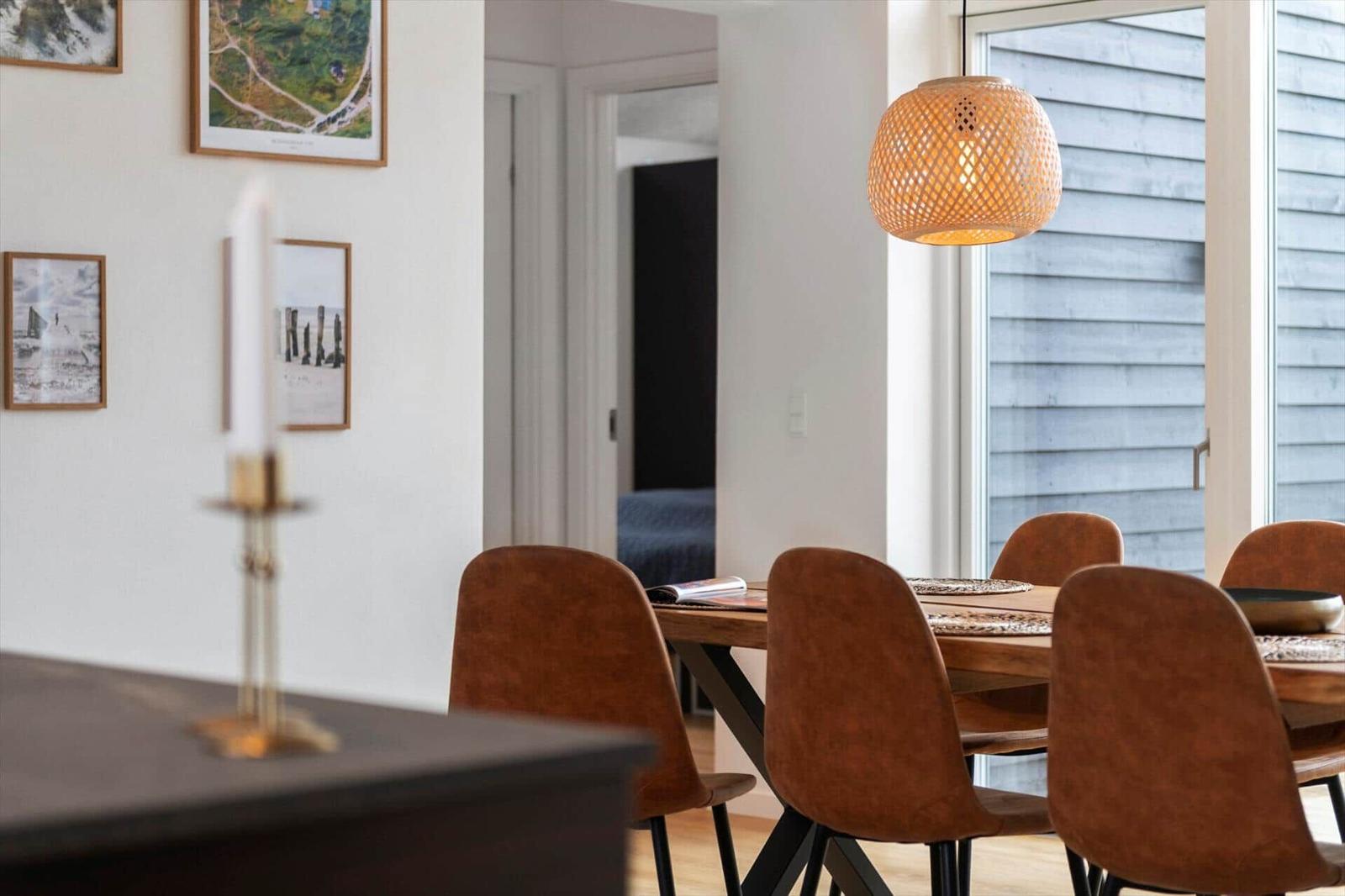 Esstisch mit braunen Stühlen und hängender Lampe. Wandbilder und Fenster mit Außenansicht.
