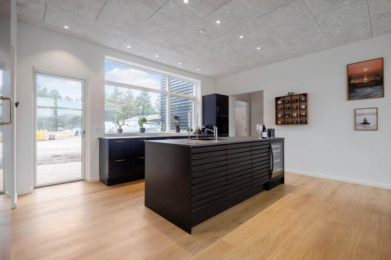 Moderne Küche mit dunklen Schränken und Holzboden. Große Fenster und Türen.
