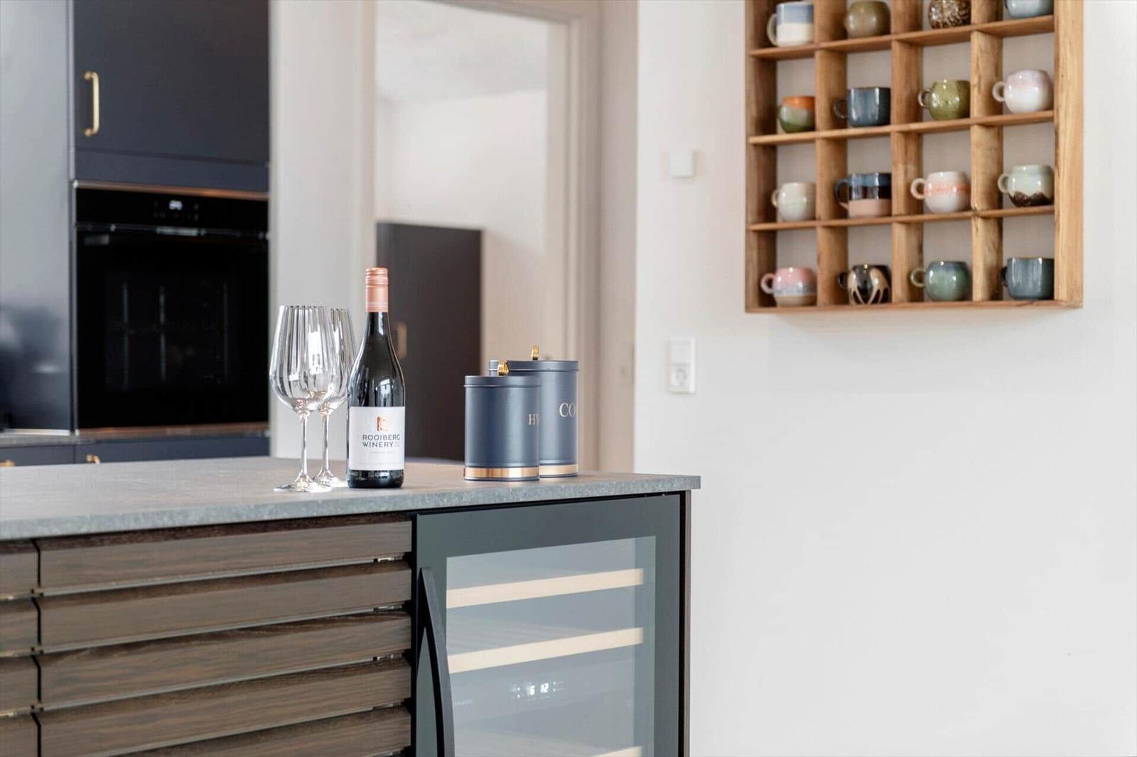 Küchenbereich mit Wein, Gläsern und Kaffeetassenregal an der Wand.
