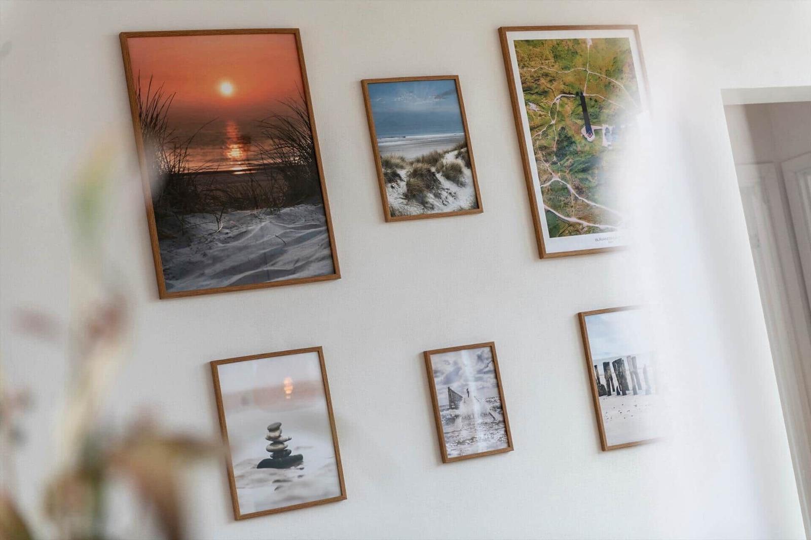 Wand mit sechs gerahmten Fotos von Küstenlandschaften und einem Leuchtturm.