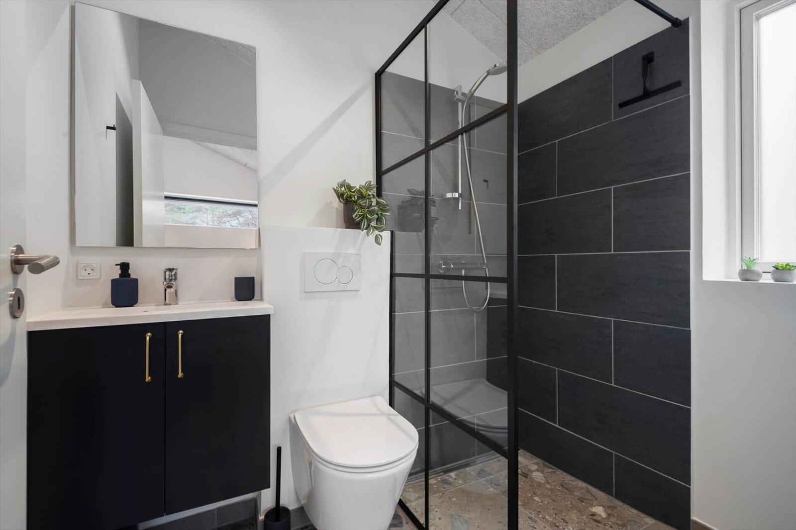 Badezimmer mit Dusche, Waschbecken und Toilette. Schwarze Fliesen und Spiegelschrank.
