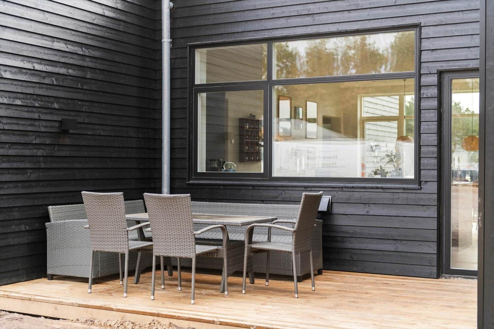 Terrasse mit Sitzgruppe vor schwarzem Holzhaus mit Fenster und Tür.
