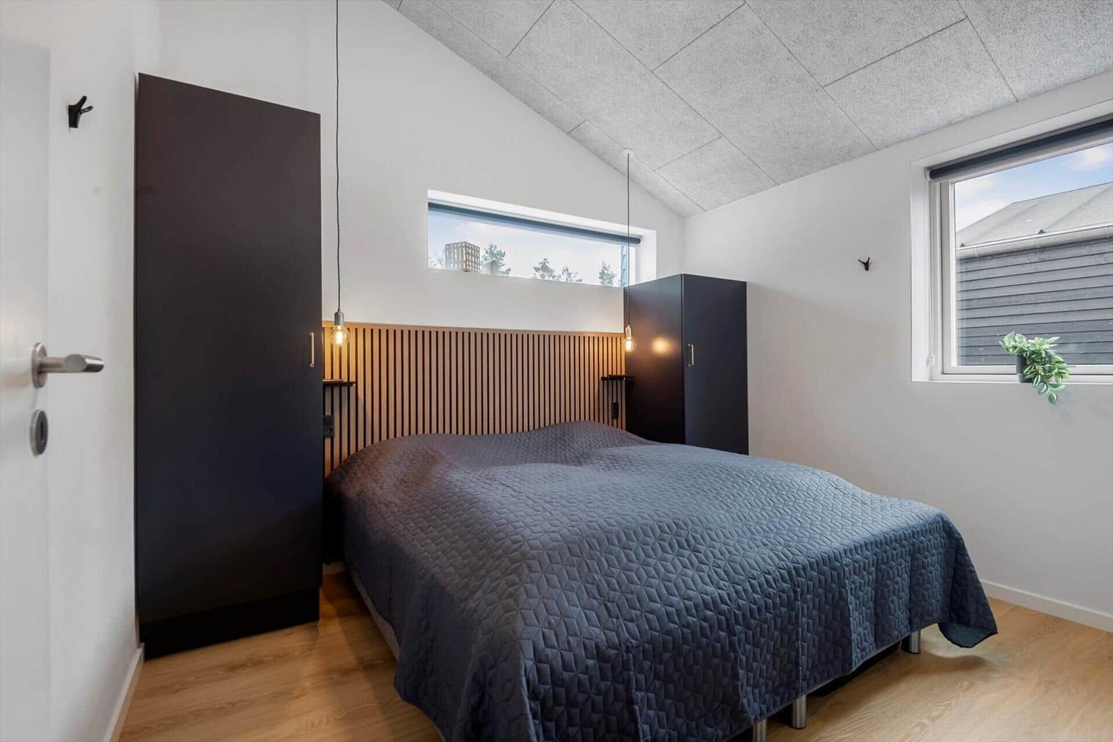 Schlafzimmer mit Bett, Kleiderschränken und Fenstern. Holzfußboden und schräger Deckenbereich.