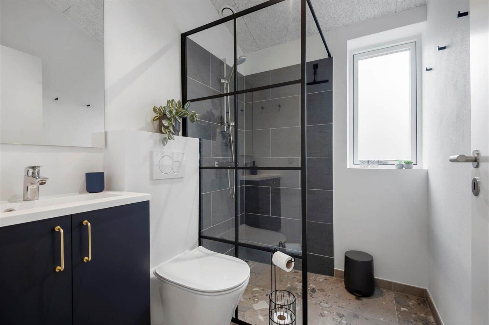 Badezimmer mit Dusche, Waschbecken und Toilette. Schwarze Fliesen und goldene Griffbügel.