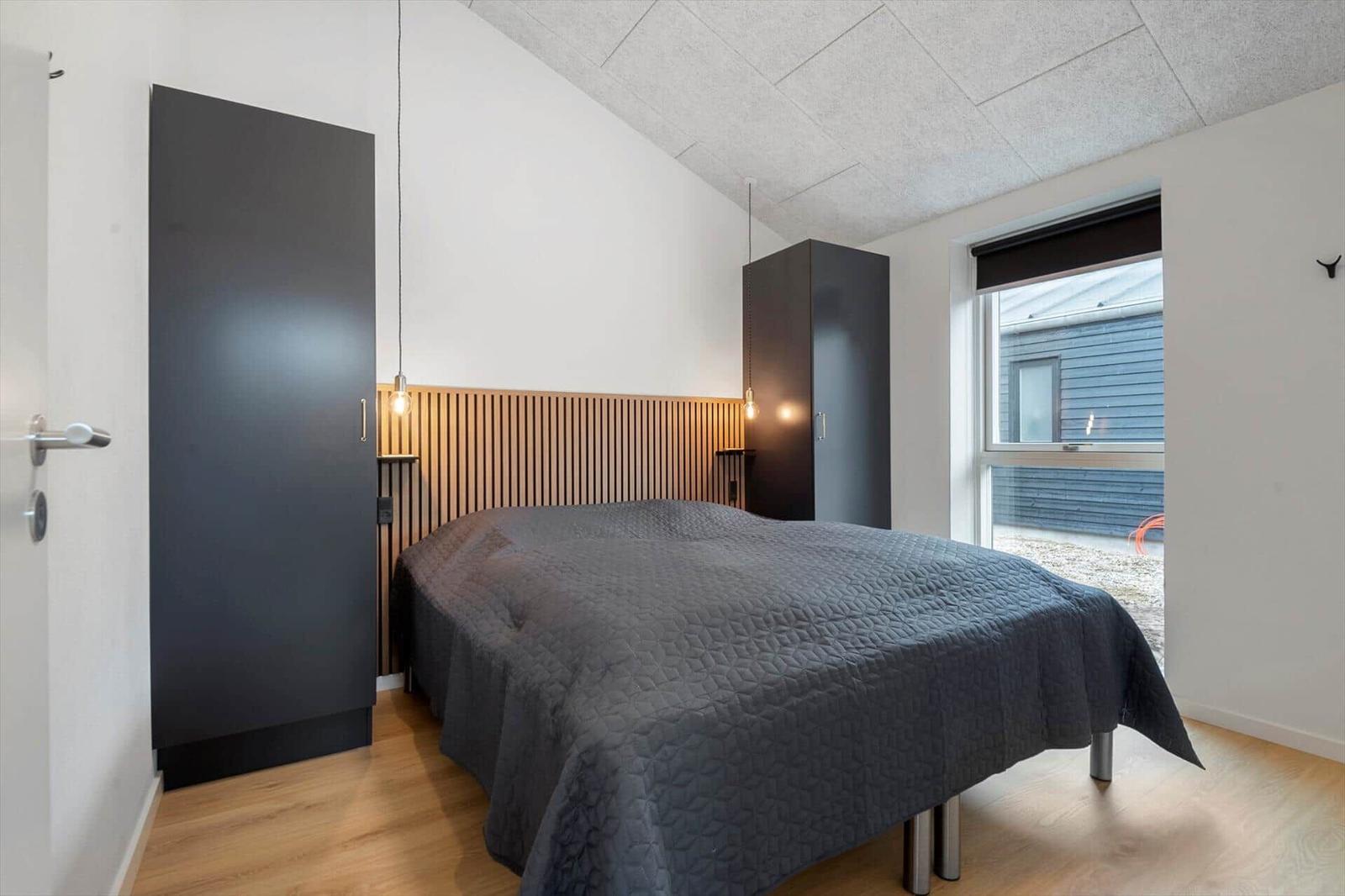 Schlafzimmer mit Bett, zwei Schränken und Holzpaneelen an der Wand.