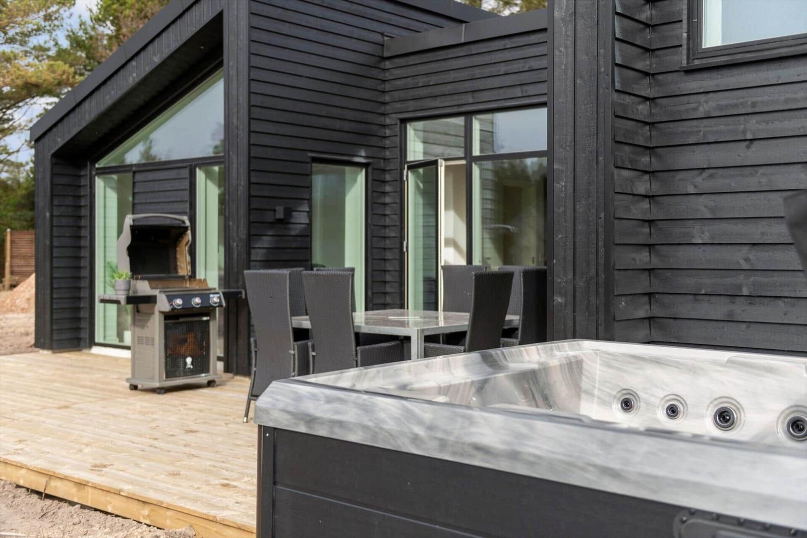 Außenbereich mit Whirlpool, Grill und Sitzgruppe vor einem modernen Haus.