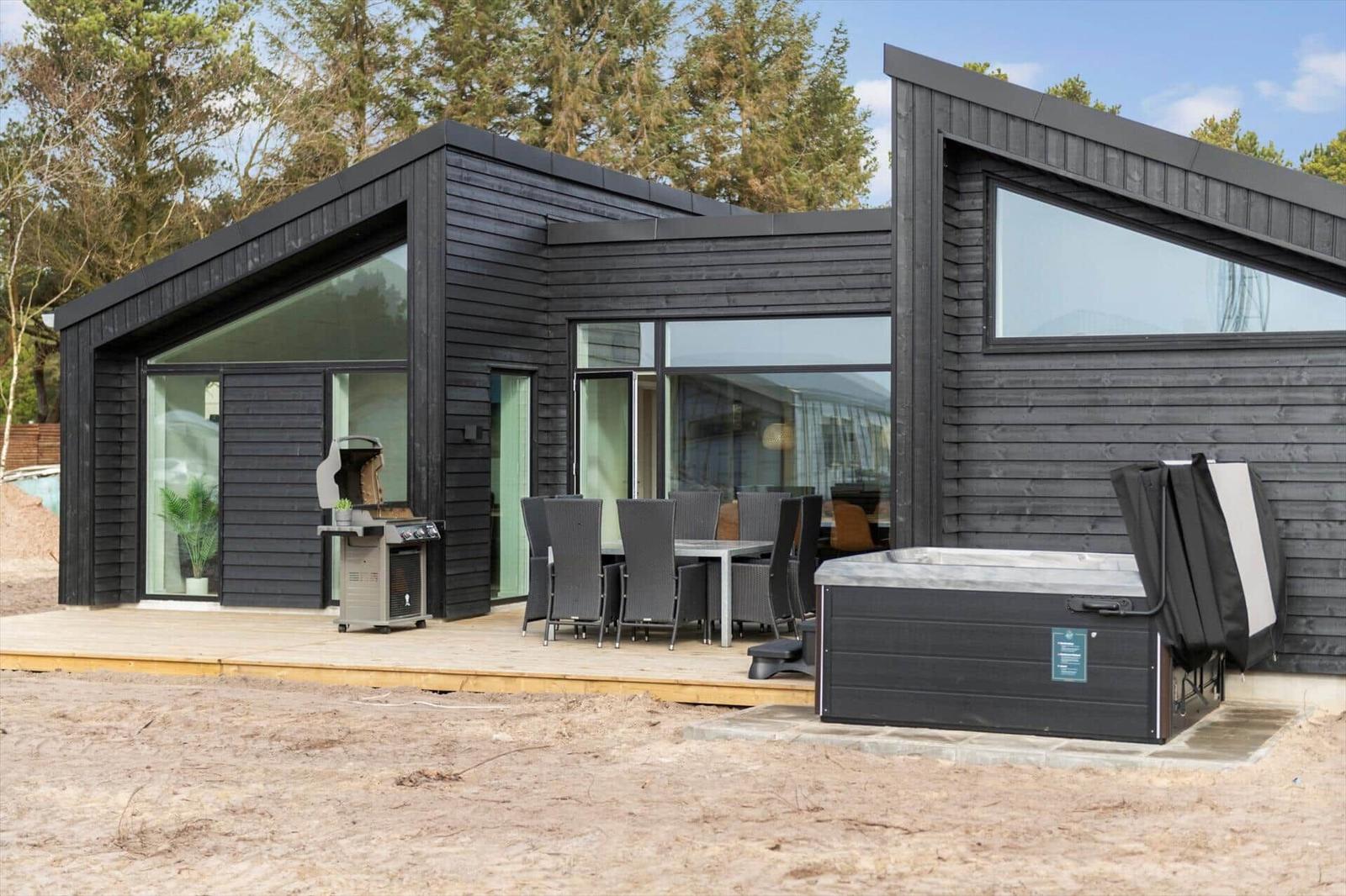 Moderne Holzhütte mit Terrasse, Grill und Whirlpool im Freien.