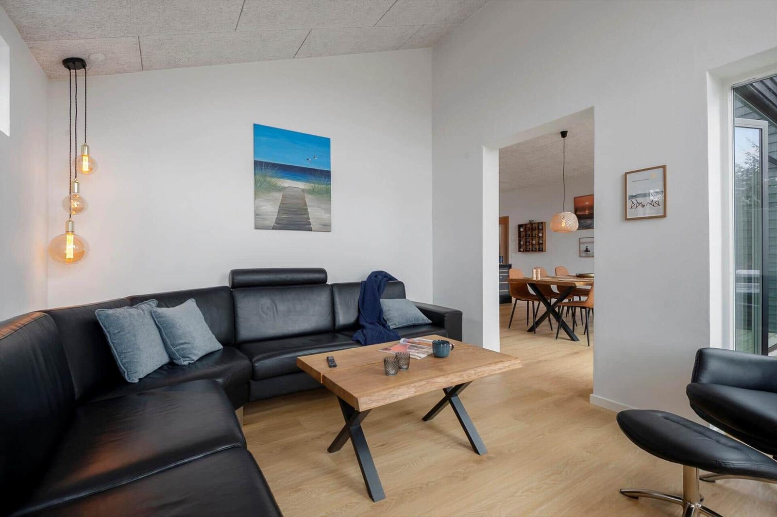 Wohnzimmer mit schwarzer Ledercouch, Holztisch und Wandbild. Durchgang zur Essnische.