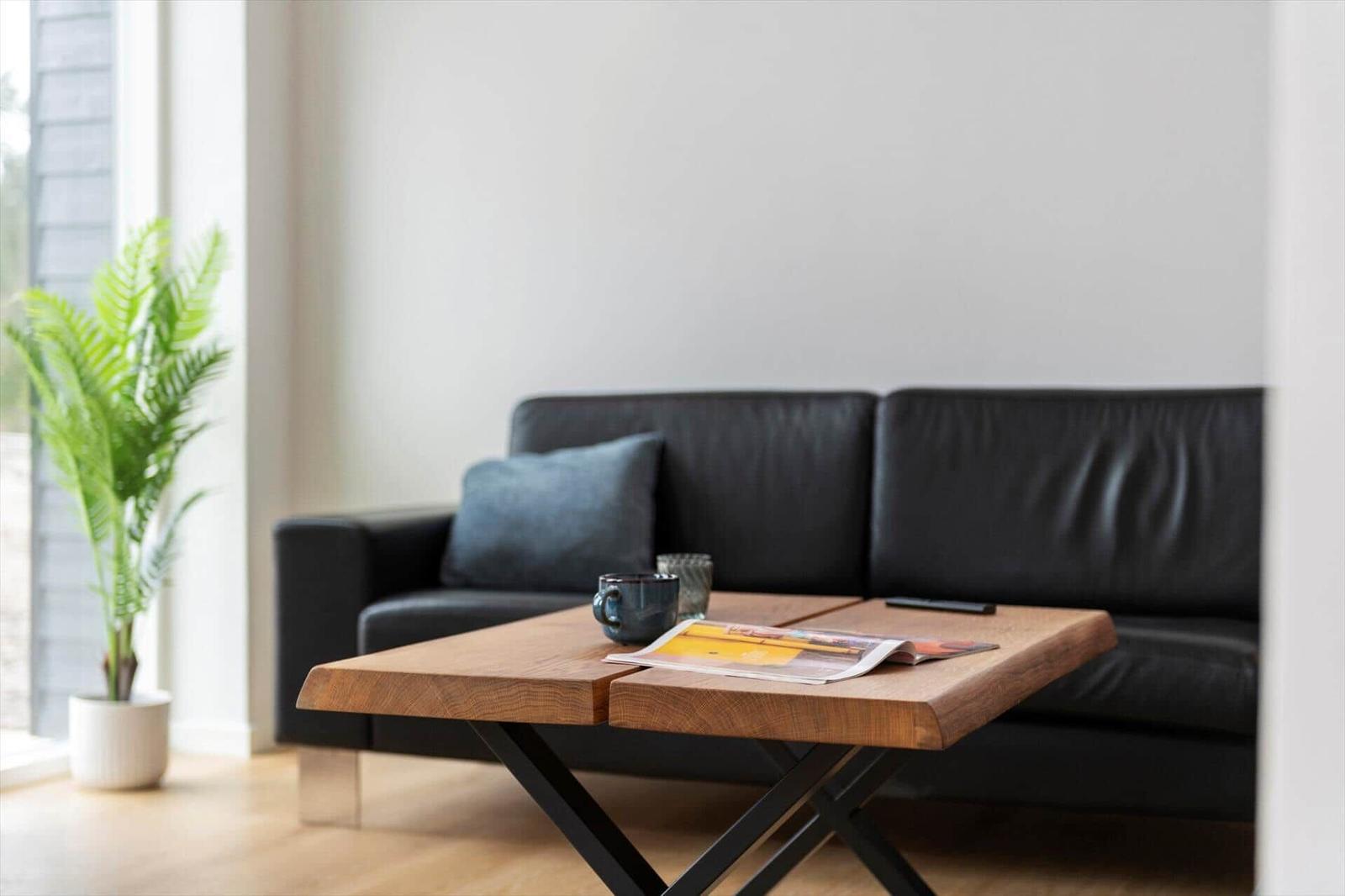 Schwarzes Sofa mit Kissen, Holztisch und Pflanze im Wohnbereich.