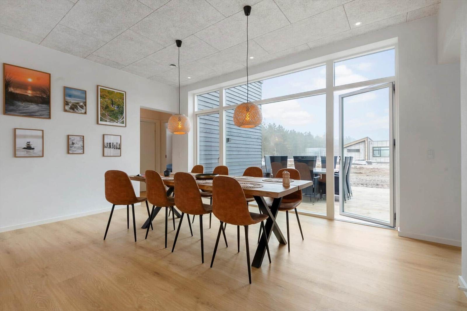 Esszimmer mit Holzboden, Tisch und Stühlen, großen Fenstern und Wandbildern.