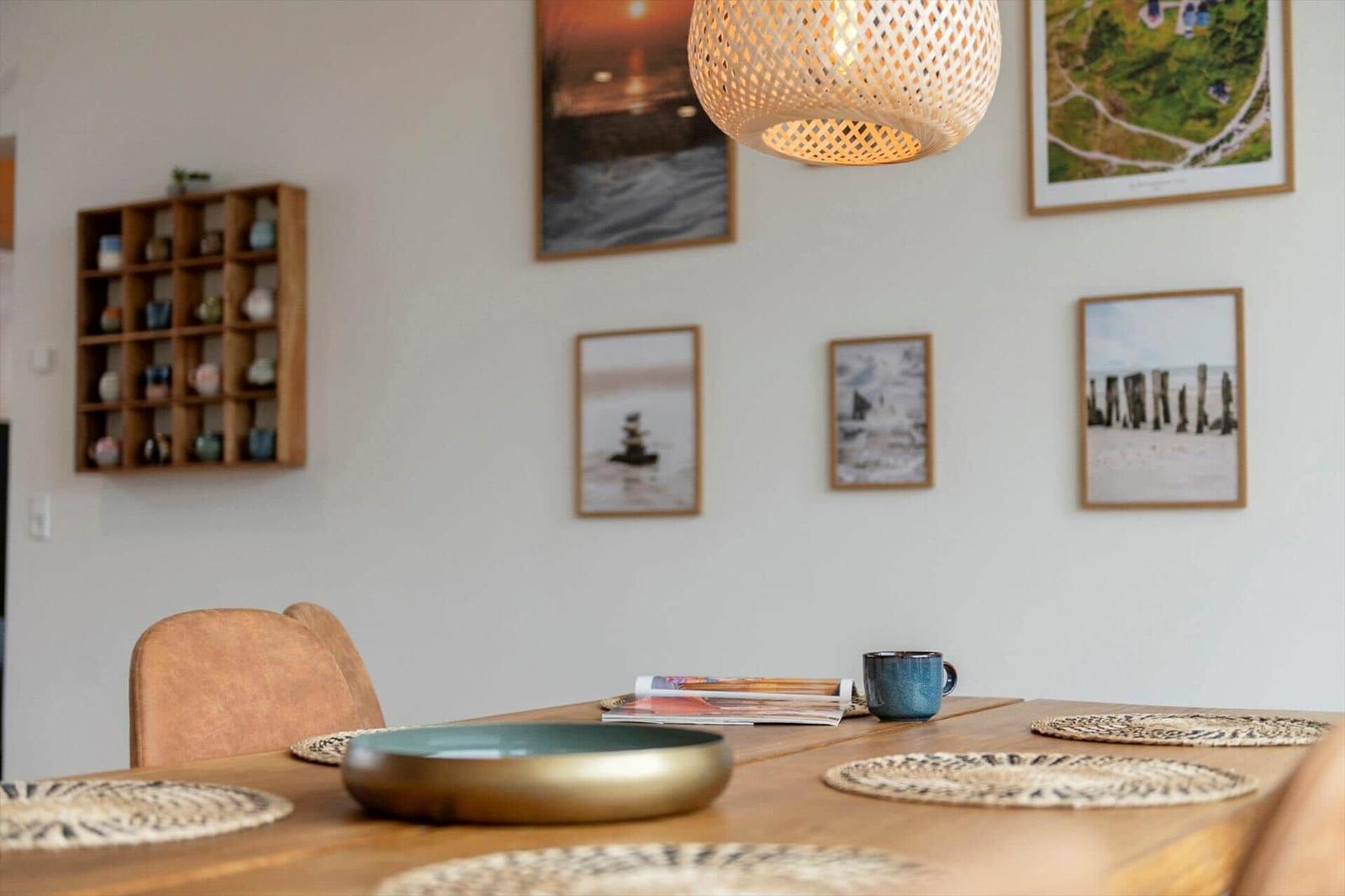 Esszimmer mit Holztisch, Stühlen und Wandbildern. Deckenleuchte und Tischmatte sichtbar.