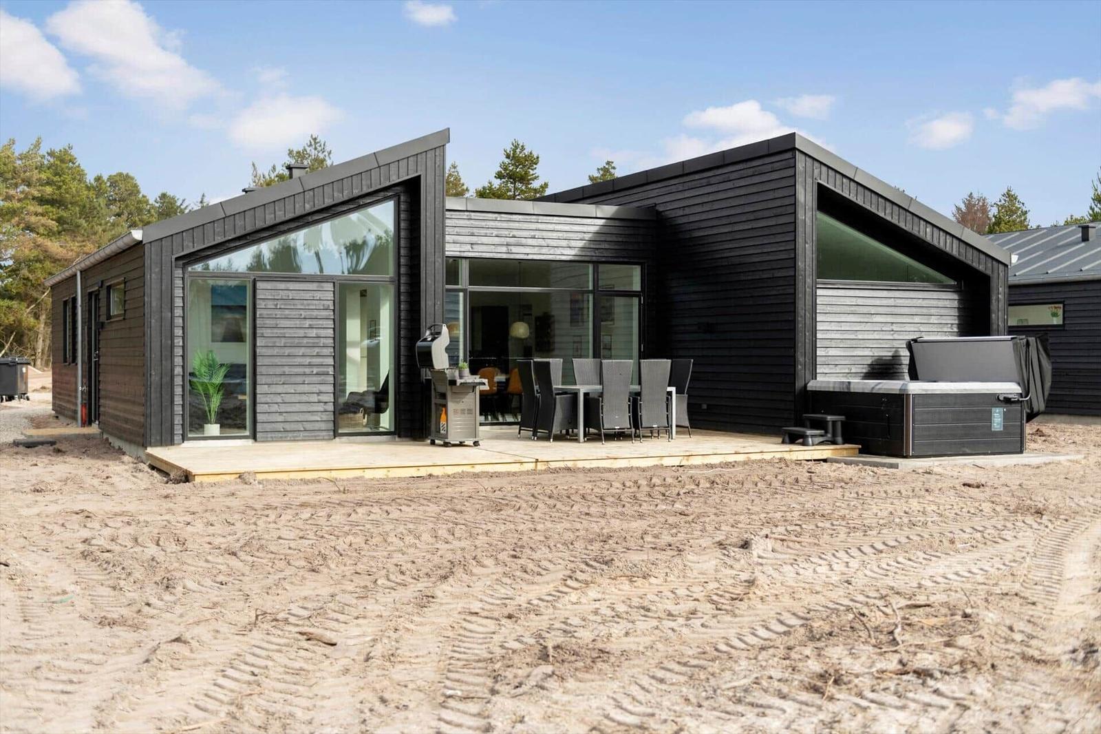 Moderne Holzhütte mit Terrasse, Grill und Whirlpool im Freien.