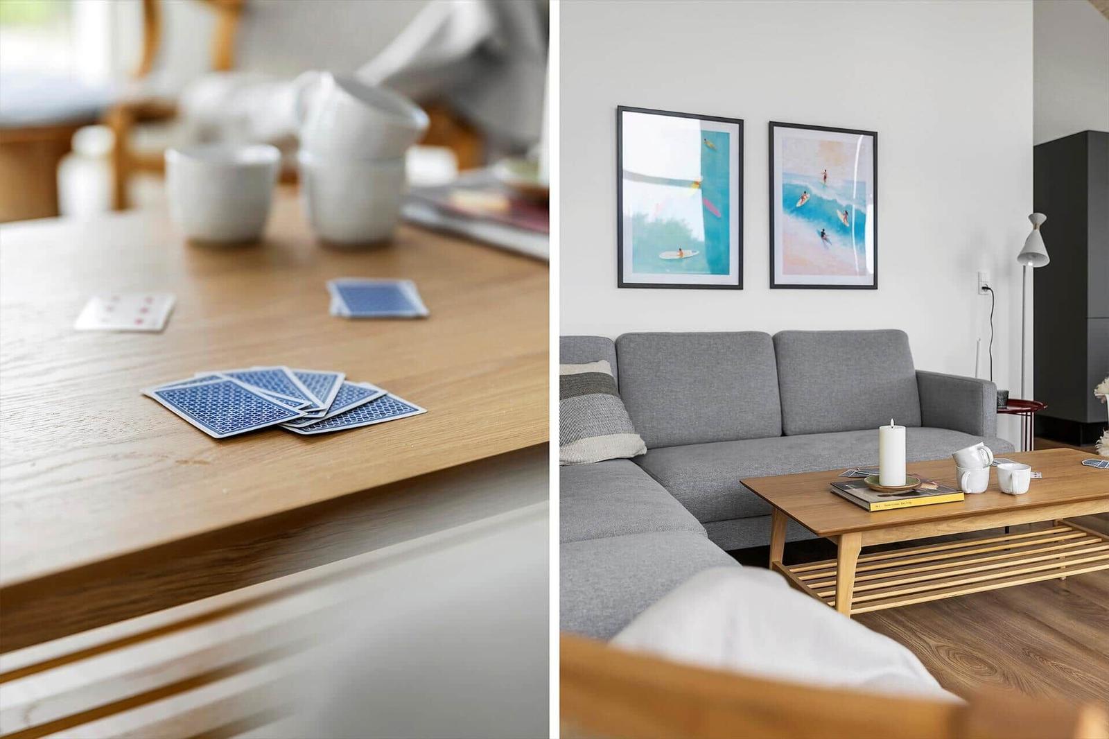 Holztisch mit Spielkarten und Tassen. Wohnzimmer mit grauem Sofa, Holzcoffee-Tisch und Wandbildern.