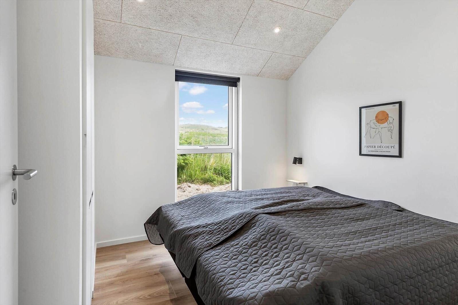 Schlafzimmer mit Blick auf Grasland, graues Bett und Wandbild.