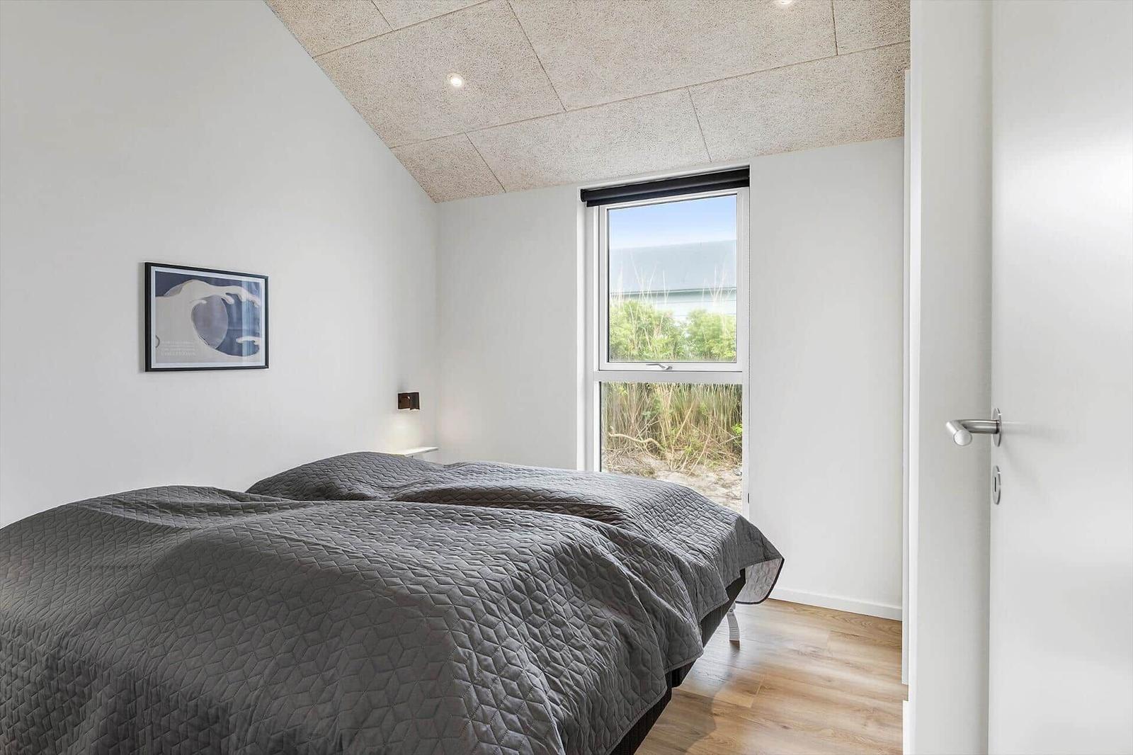 Schlafzimmer mit Bett, Fenster und Holzboden. Wandbild und Deckenleuchte sichtbar.