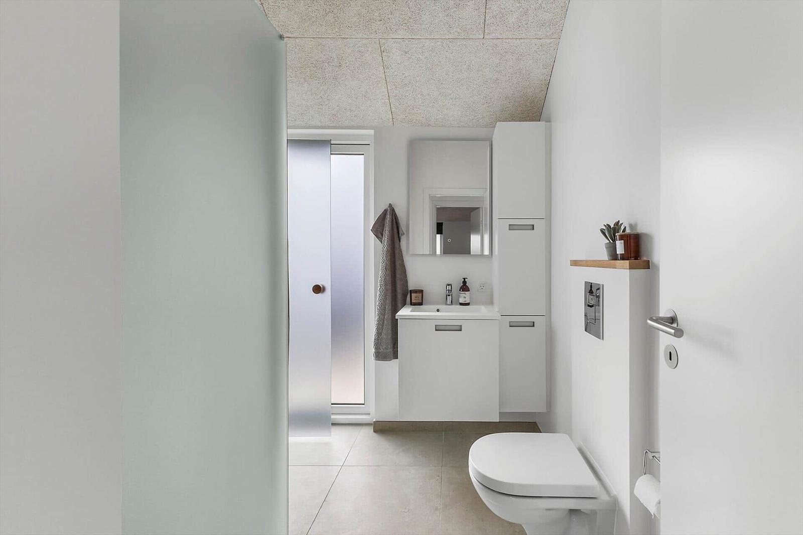 Badezimmer mit Toilette, Waschbecken und Spiegel. Dusche mit Glaswand.
