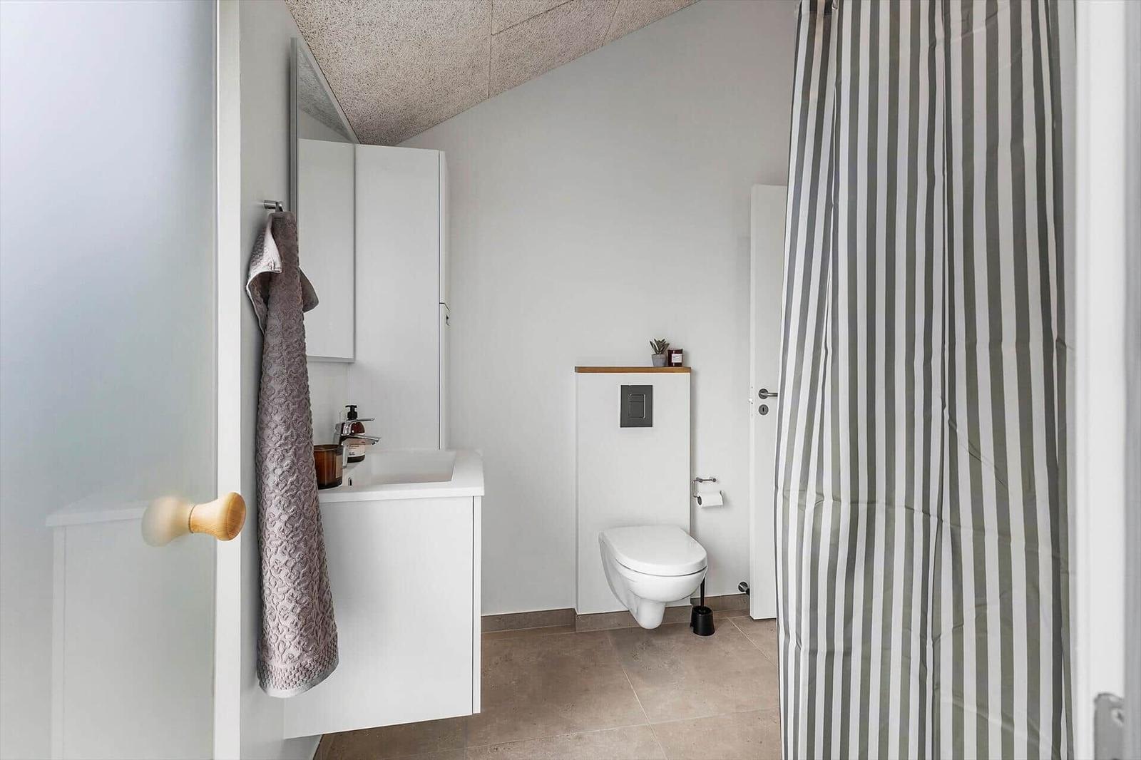 Badezimmer mit Waschbecken, Toilette und Dusche mit Streifenvorhang.