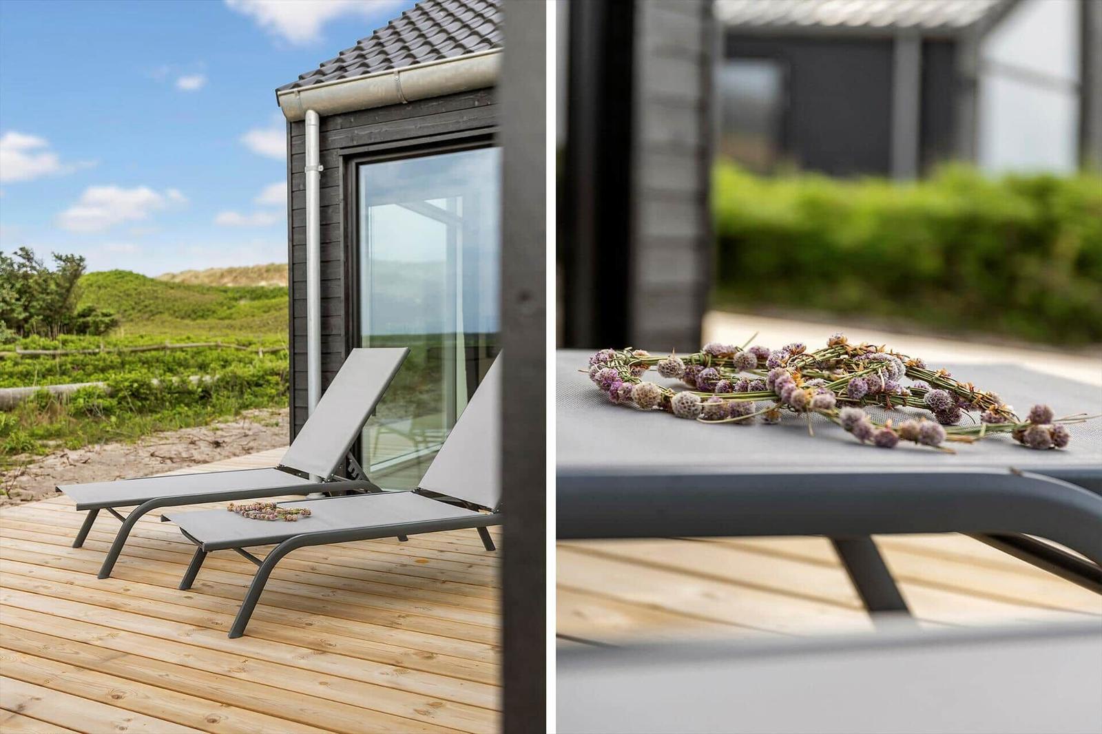 Zwei Liegestühle auf Holzterrasse vor modernem Haus mit Blick auf Grünland.