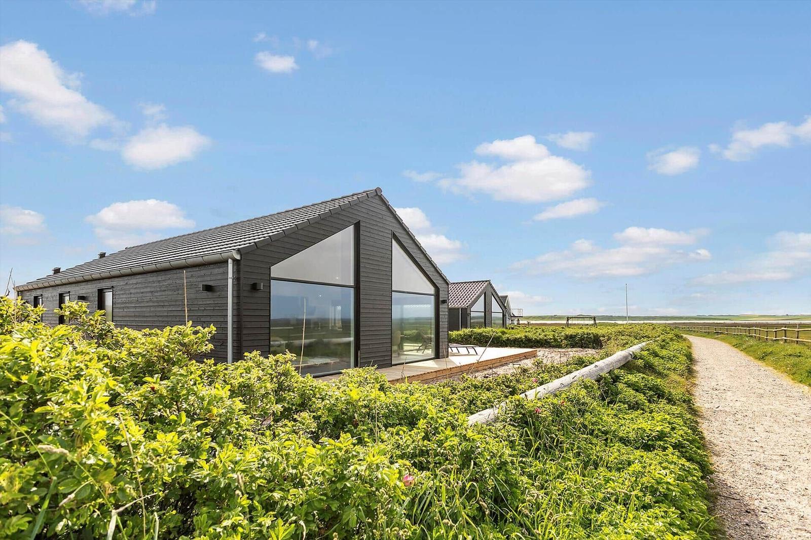 Moderne Holzhäuser mit großen Glasfronten in einer grünen Landschaft unter blauem Himmel.