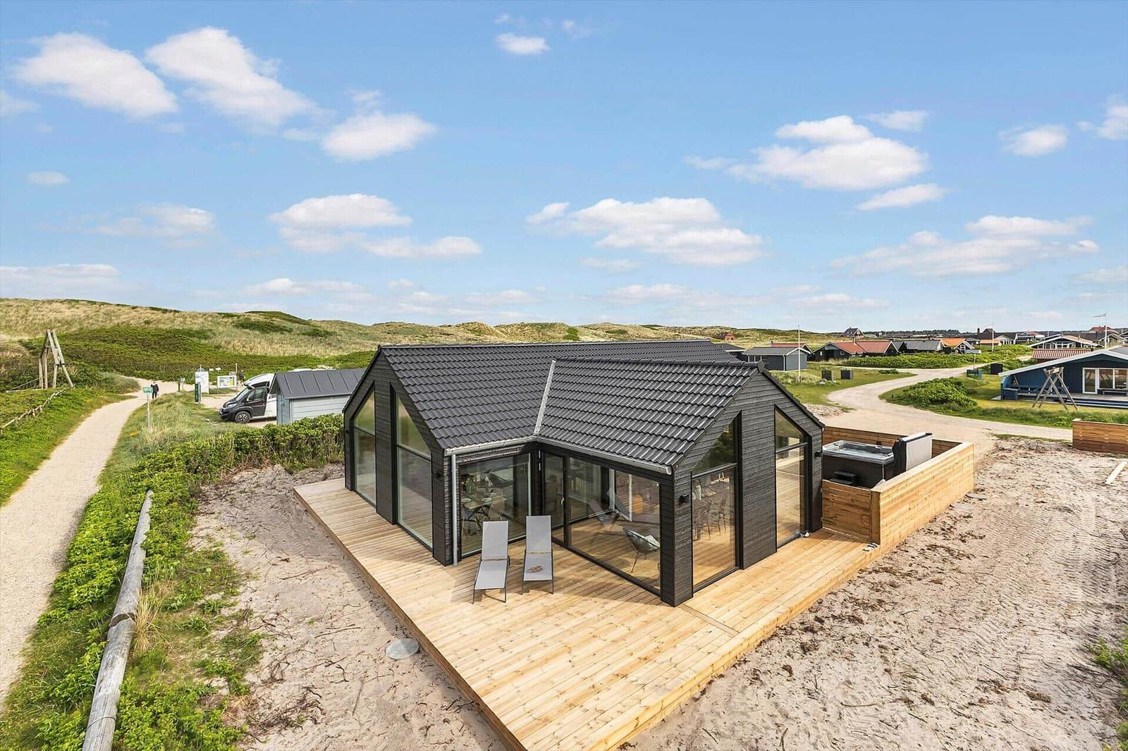 Moderne Strandhütte mit Holzterrasse und Glasfassade. Blick auf Dünen und Strand.