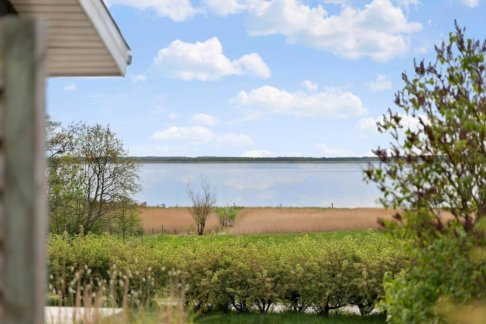 From the terrace, a calm lake with grassland and trees is visible.
