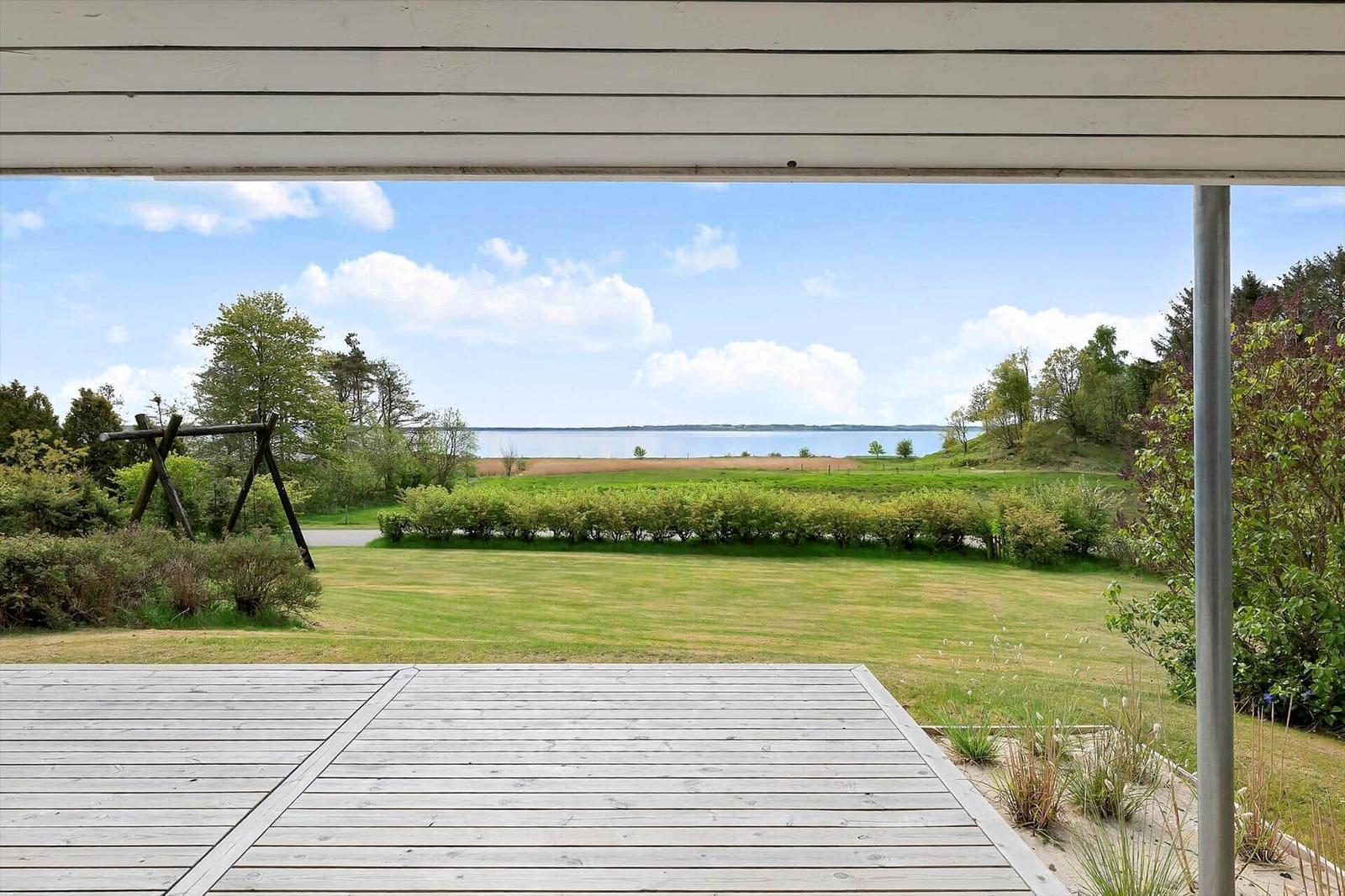 Deck with view of green field and lake under blue sky.