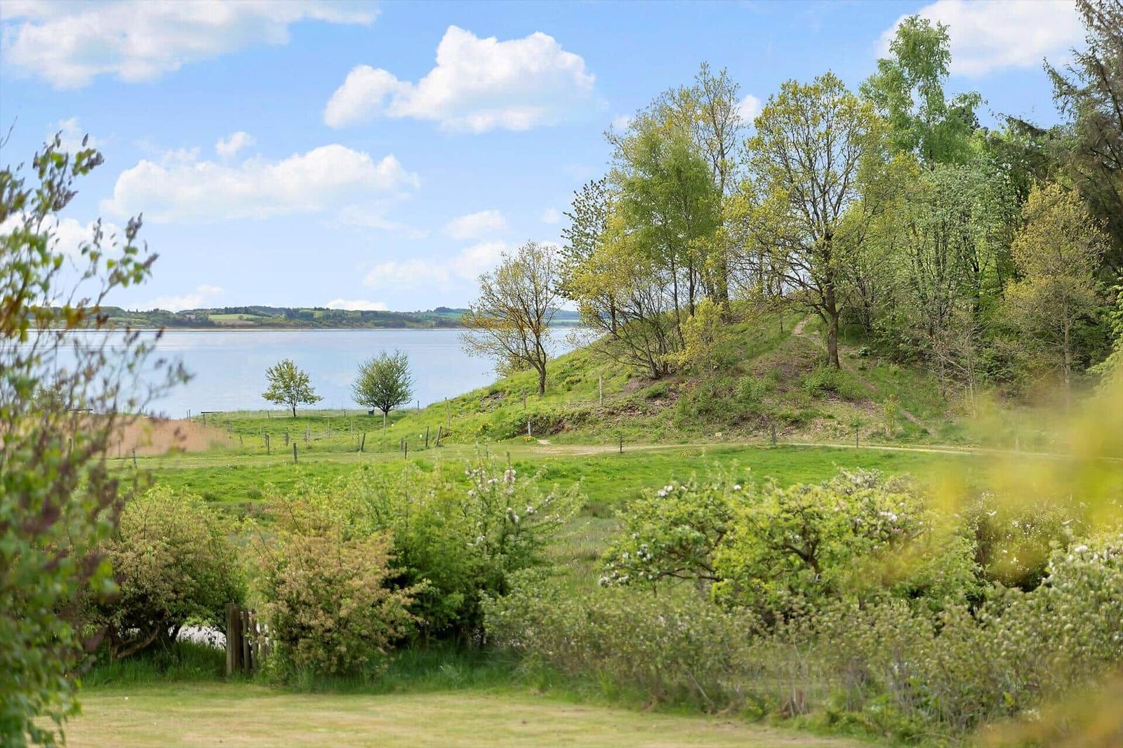 Green field with trees and a lake in the background under a blue sky.