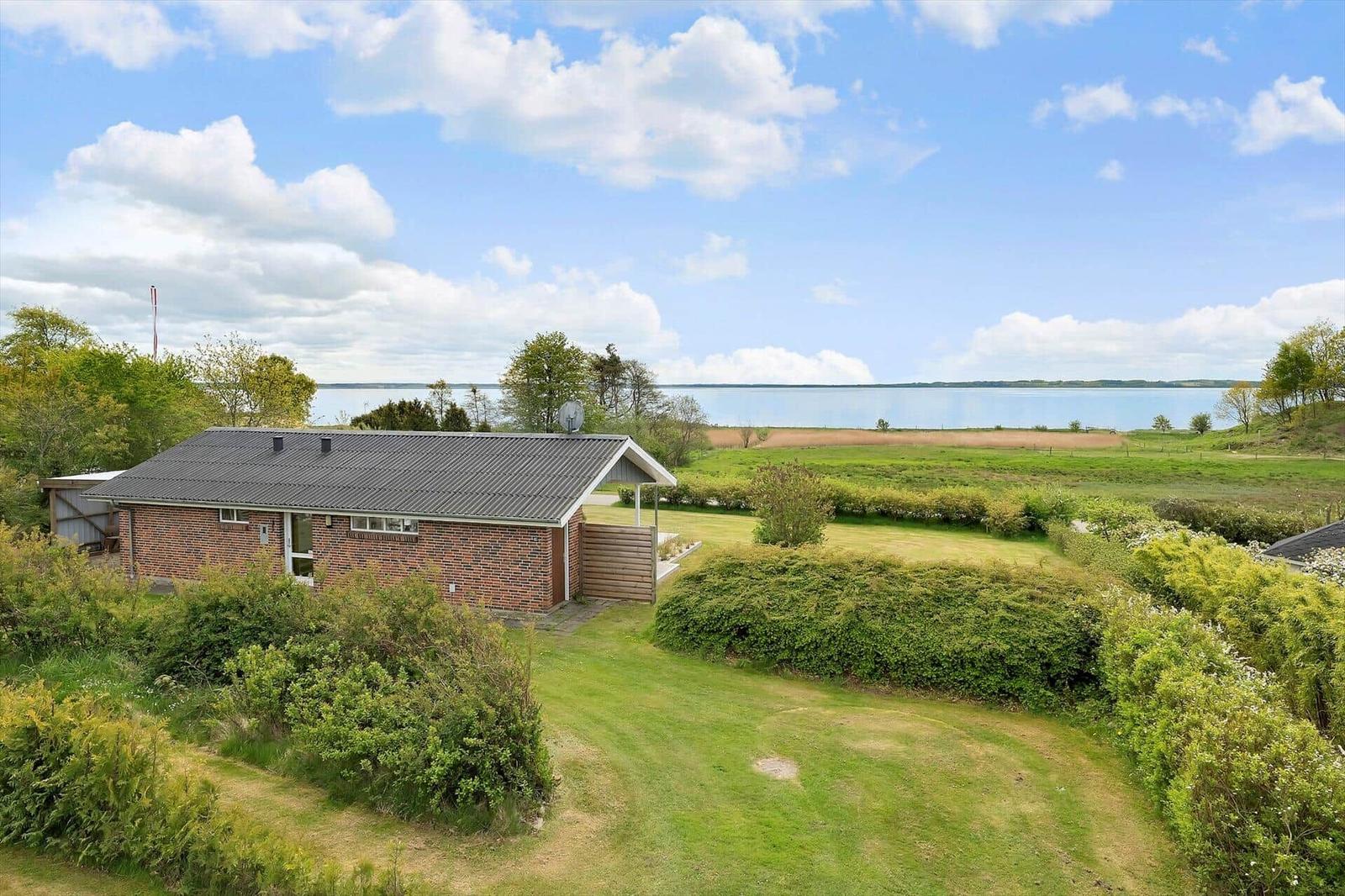 A small house with garden and view of a lake under blue sky.