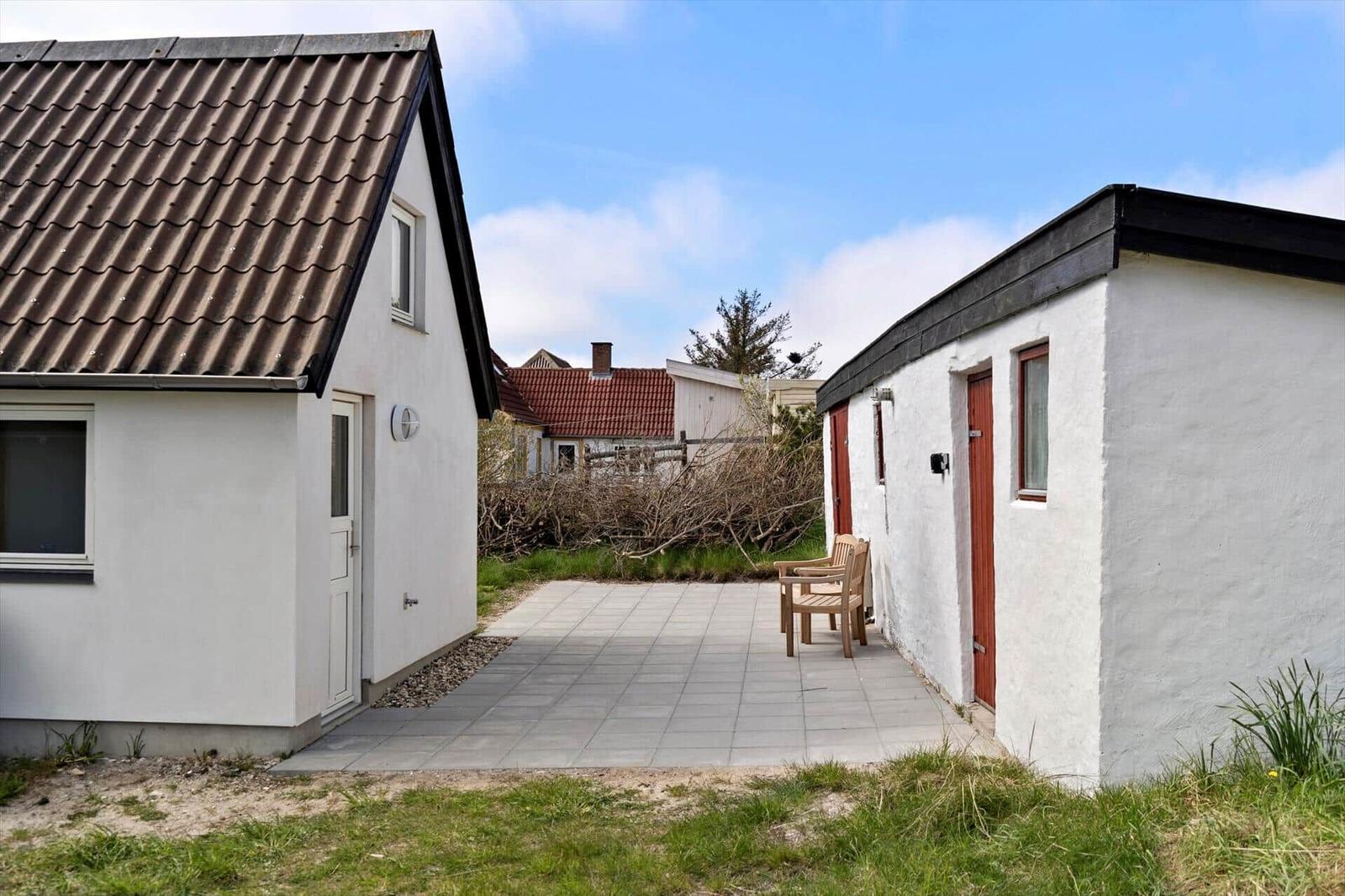 Two white houses with red doors and terrace with wooden chairs.