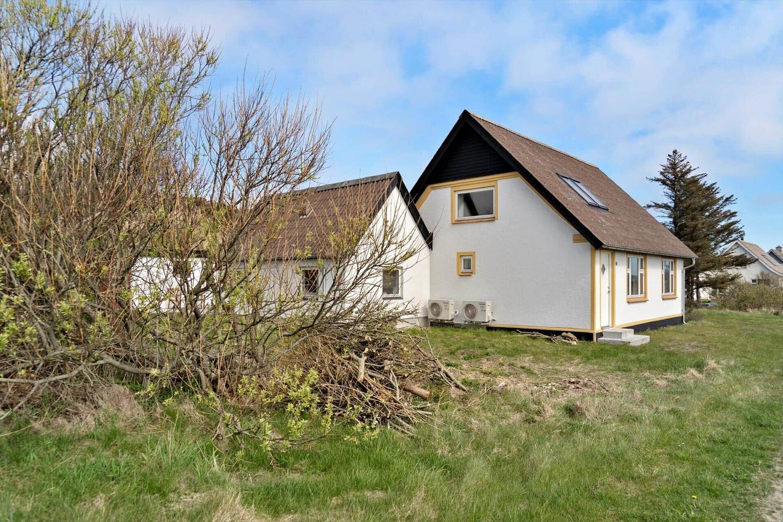 A white house with a brown roof and yellow window frames on green ground.