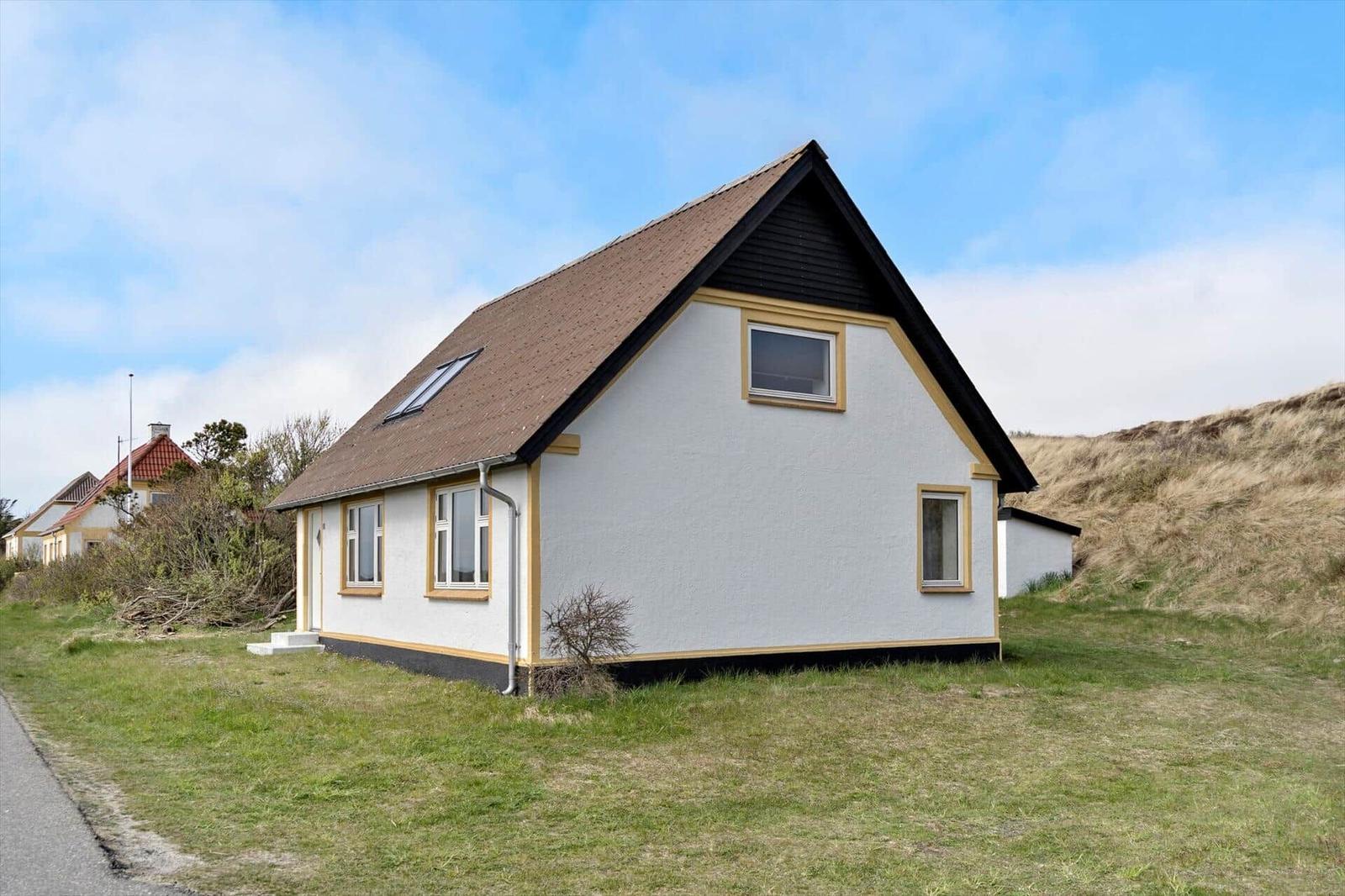 A white house with a brown roof and yellow window frames stands on a green lawn.
